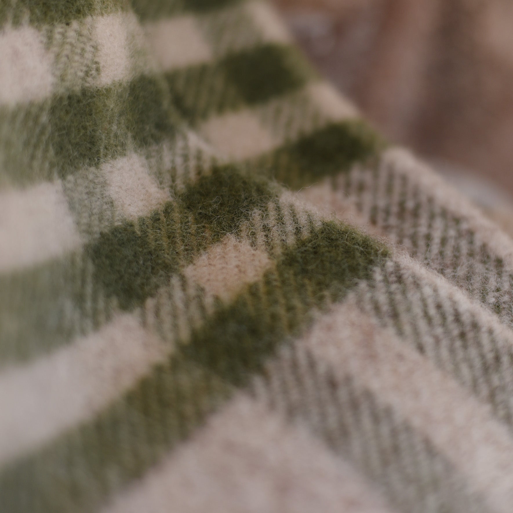 Close-up of Campbells of Beauly Tarradale Lambswool Throw, featuring a soft green and beige check pattern. The warm, cozy texture showcases classic British craftsmanship with a gently blurred edge for a timeless look.