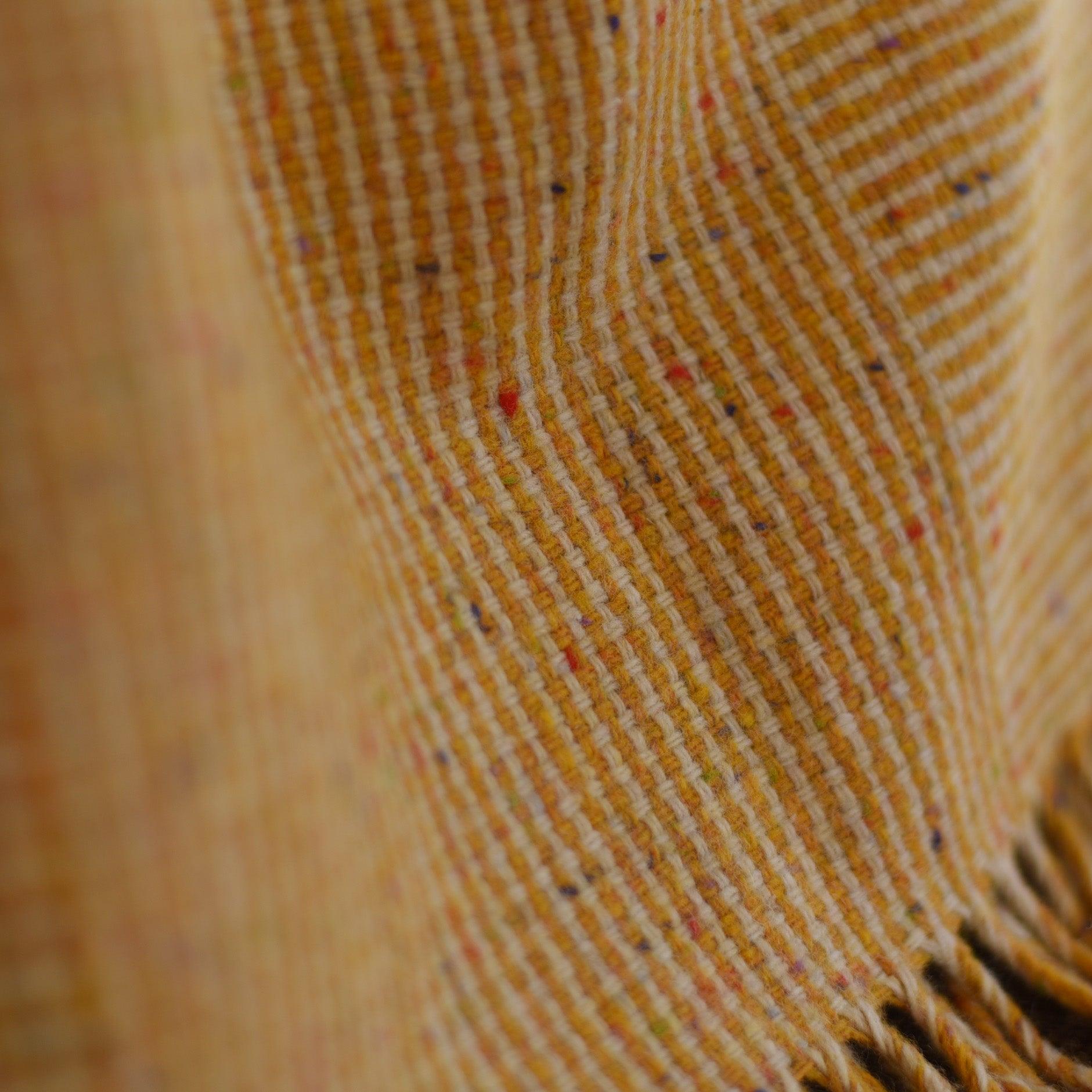 Close-up of the Cabrich Lambswool Throw by Campbells of Beauly, featuring yellow and orange hues, fine lines, colorful flecks, and soft folds for a textured, cozy look inspired by traditional Donegal wool.