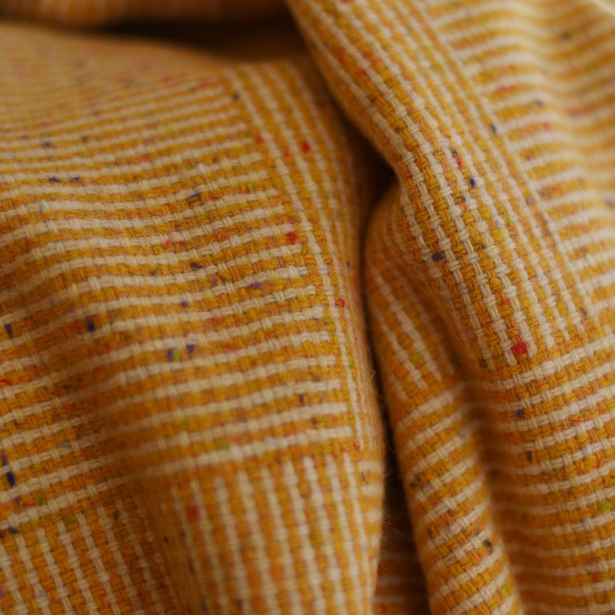 Close-up of the Cabrich Lambswool Throw by Campbells of Beauly: yellow ribbed fabric with fine horizontal lines and multicolored flecks, featuring soft folds and a cozy, textured appearance.