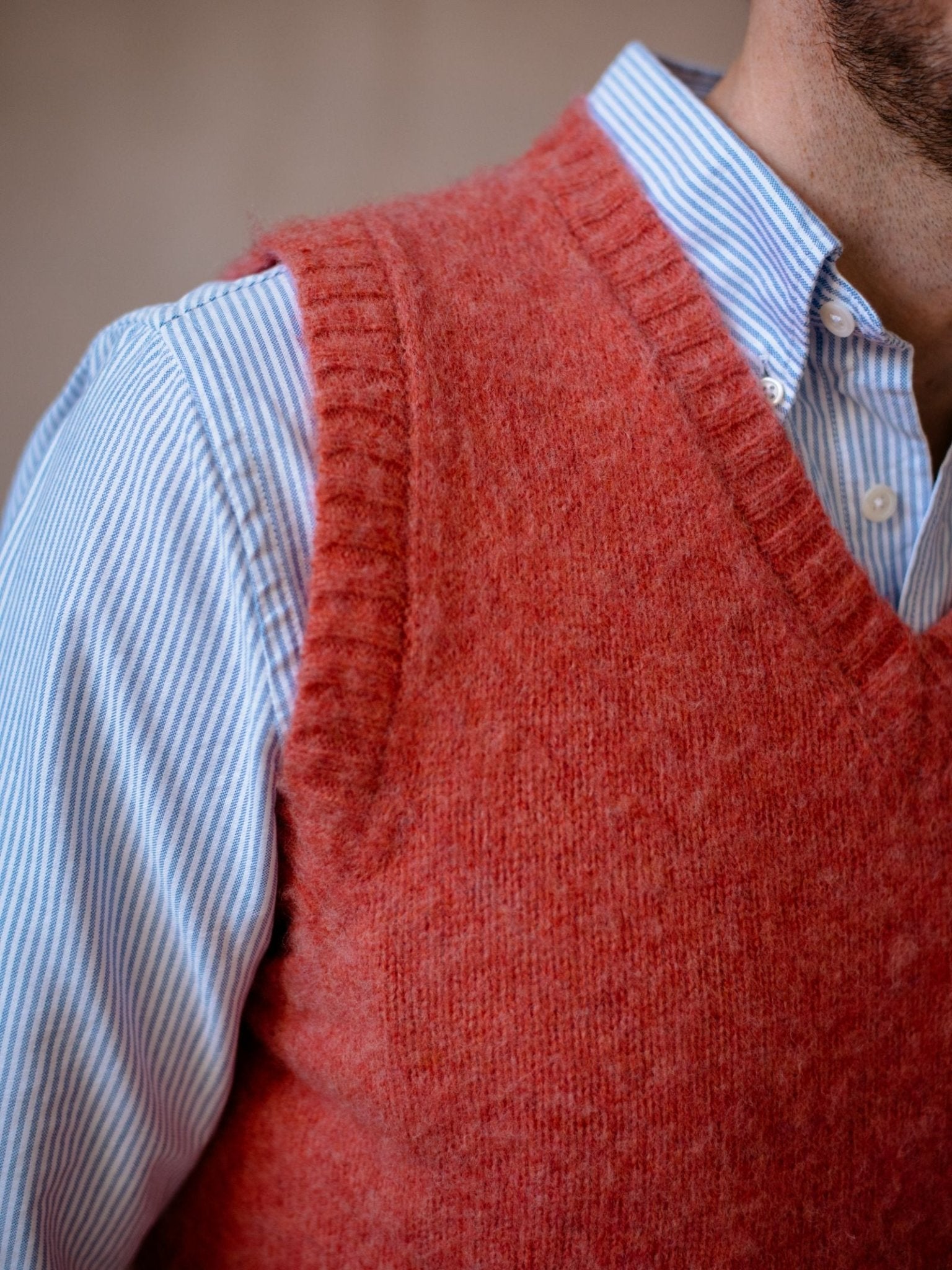 Close-up of a person wearing the Campbells of Beauly Shetland Slipover, a textured, fuzzy wool V-neck sweater vest layered over a light blue and white striped button-up shirt. Only the upper torso, neck, and shoulder are visible.