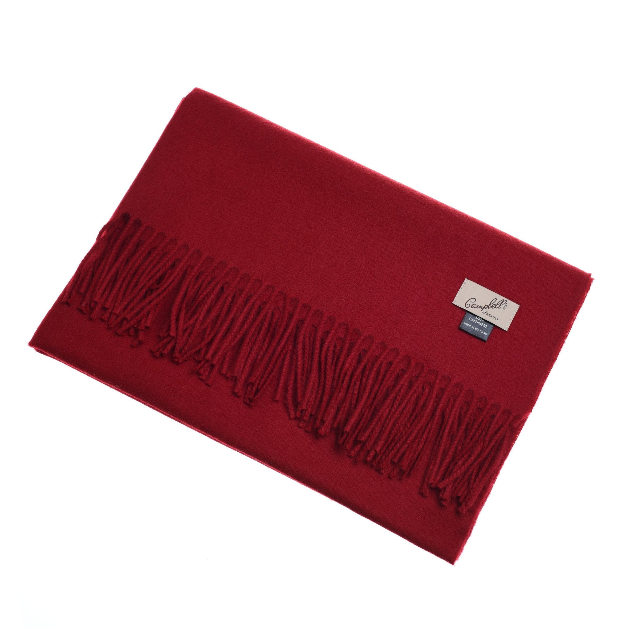 A deep red Campbells of Beauly Cashmere Stole, crafted from fine cashmere yarns with fringe on one edge and two sewn labels (beige and black), is shown folded against a white background.