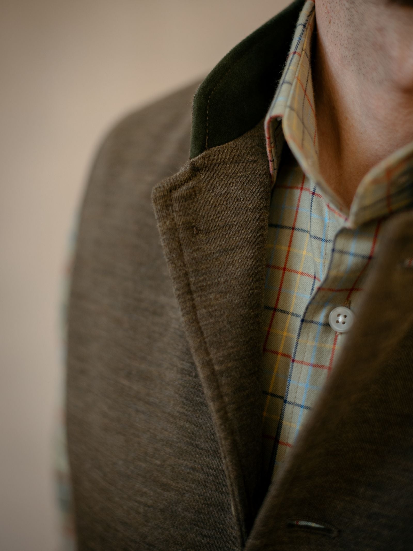 Close-up of a person wearing Campbells of Beauly Knitted Nehru Gilet over a light plaid shirt with red, blue, and yellow lines; lower face and neck partially visible—a refined layering piece.
