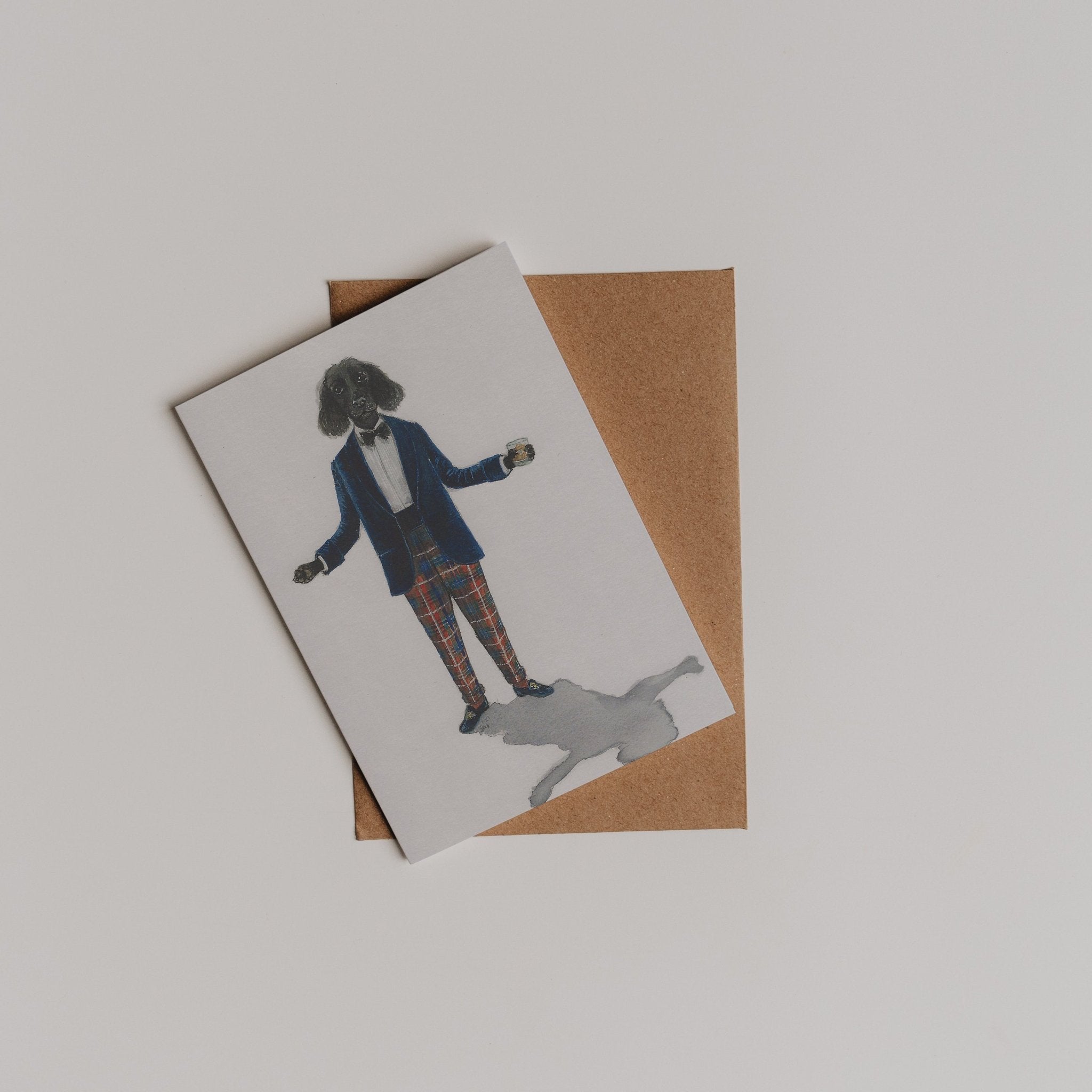 The Campbells of Beauly Evening Wear Greeting Card features a dog in a suit and plaid pants, standing atop a brown envelope on a white surface.