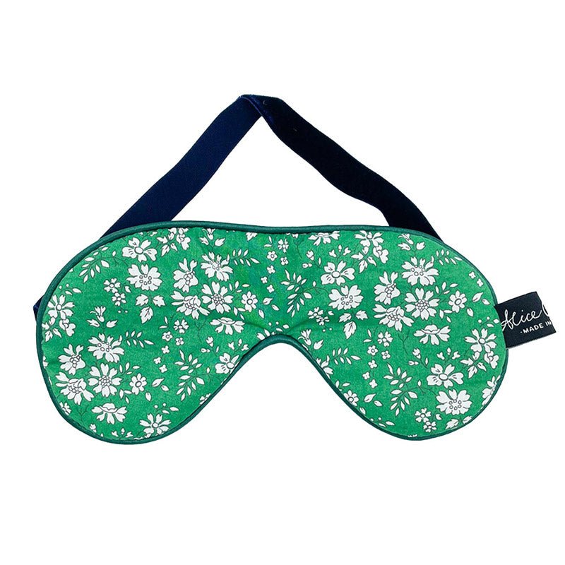 The Alice Caroline Liberty Print Eye Mask features a white floral pattern, dark trim, and a black elastic strap. Velvet padding ensures comfort, and a small black tag with white text accents the side—all shown on a white background.