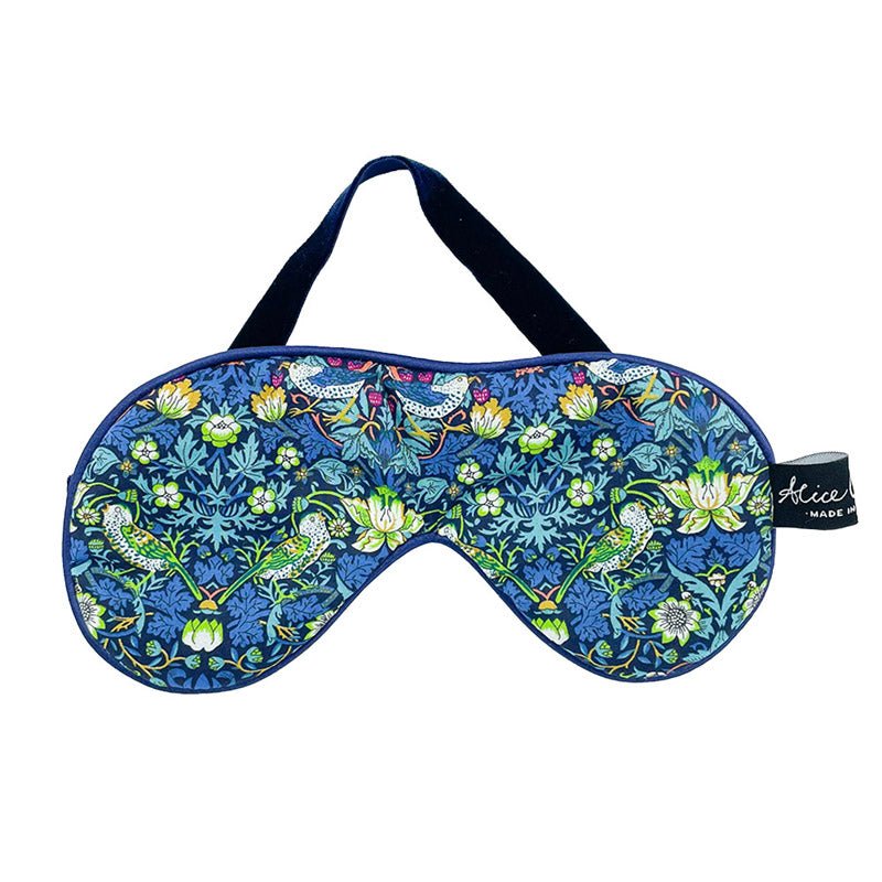 The Alice Caroline Liberty Print Eye Mask features a blue floral and bird pattern with green leaves, yellow flowers, soft velvet backing, and a black elastic strap for comfort. Tag labeled Alice.