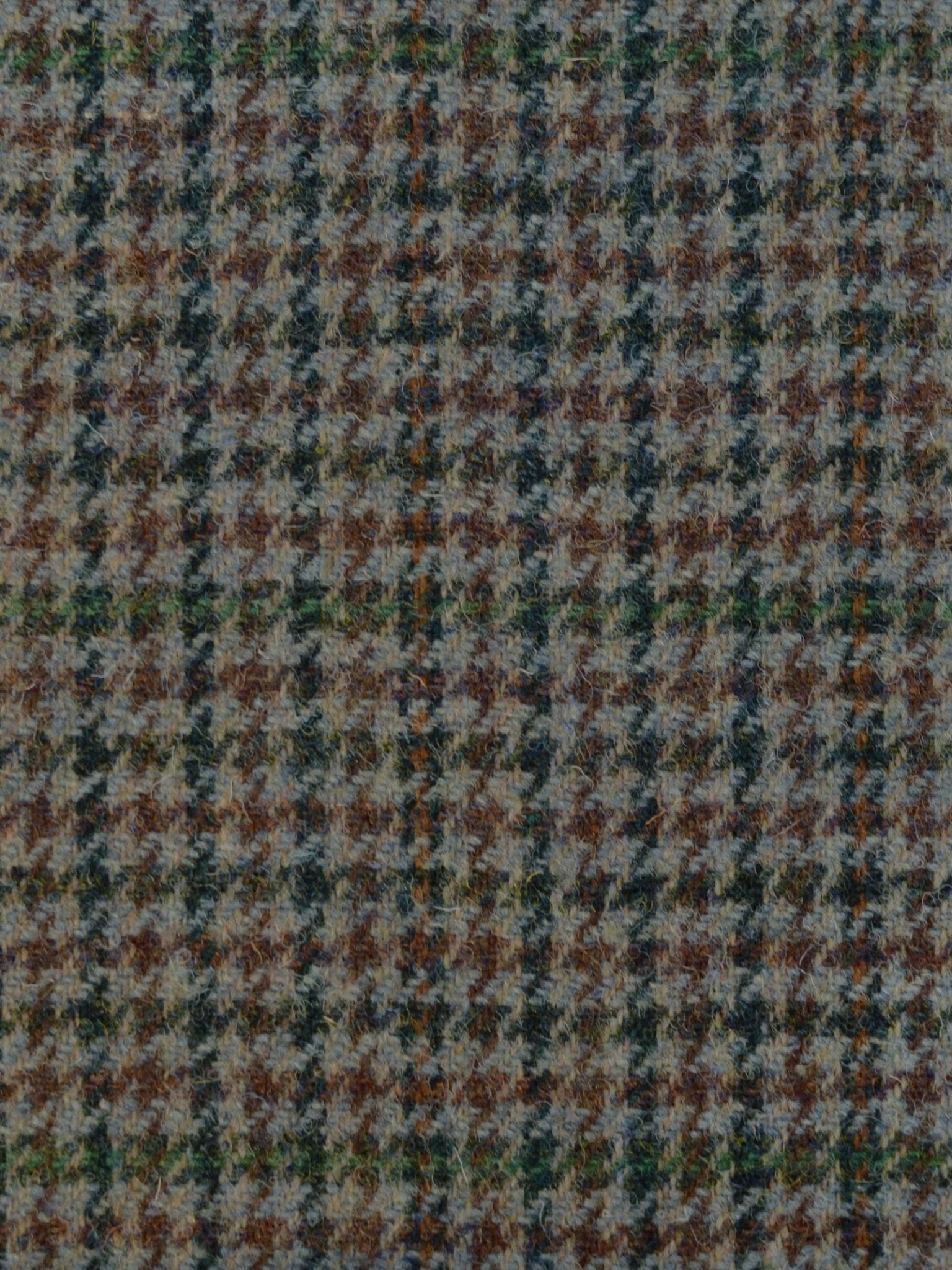 A close-up of Campbell's of Beauly House Tweed 93900, a featherweight houndstooth fabric with textured, woven shades of brown, gray, green, and blue in classic Scottish geometric patterns.
