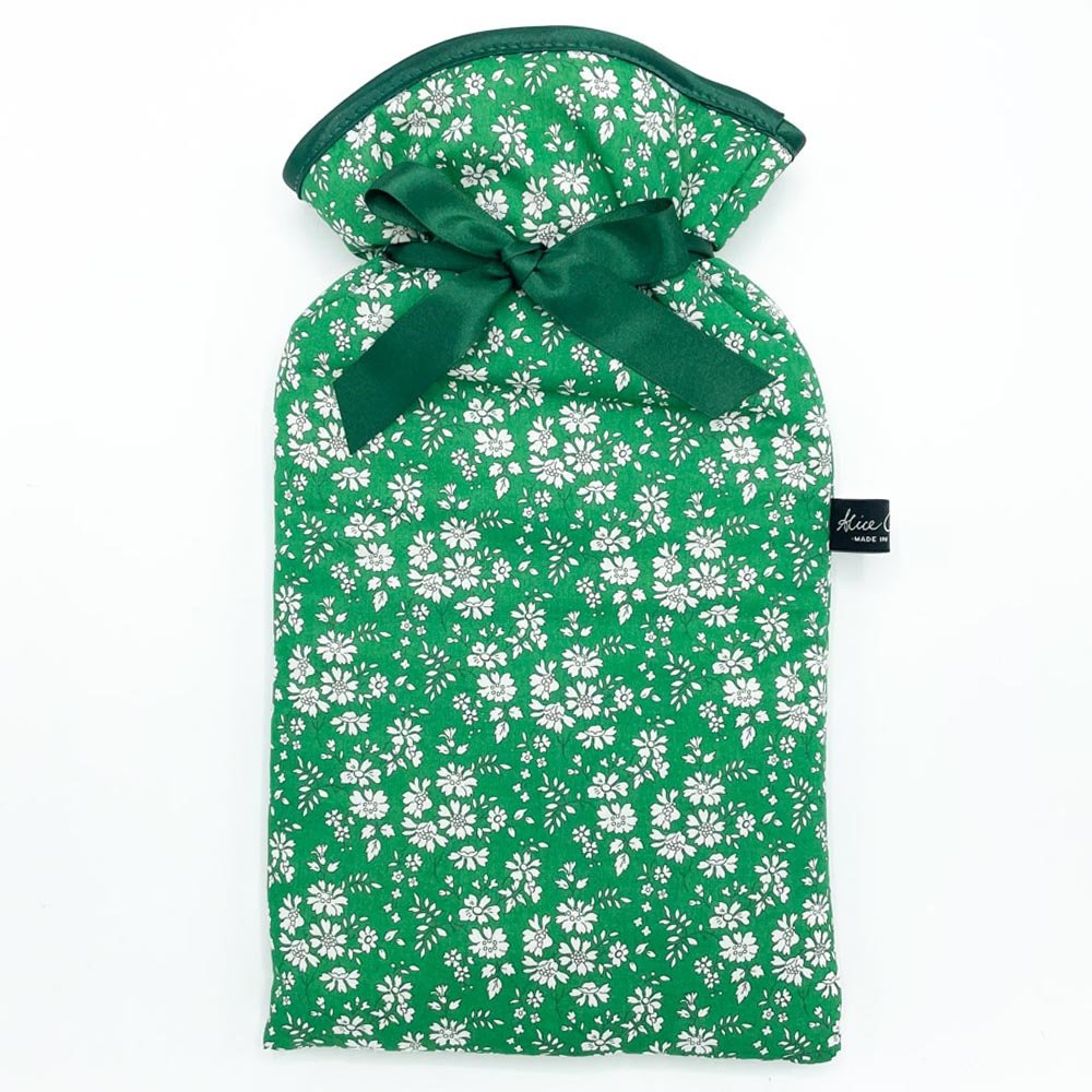 The Alice Caroline Liberty Print Hot Water Bottle features green Liberty cotton with a white floral pattern, tied with a green satin ribbon and finished with a small black Alice Caroline tag on the side.