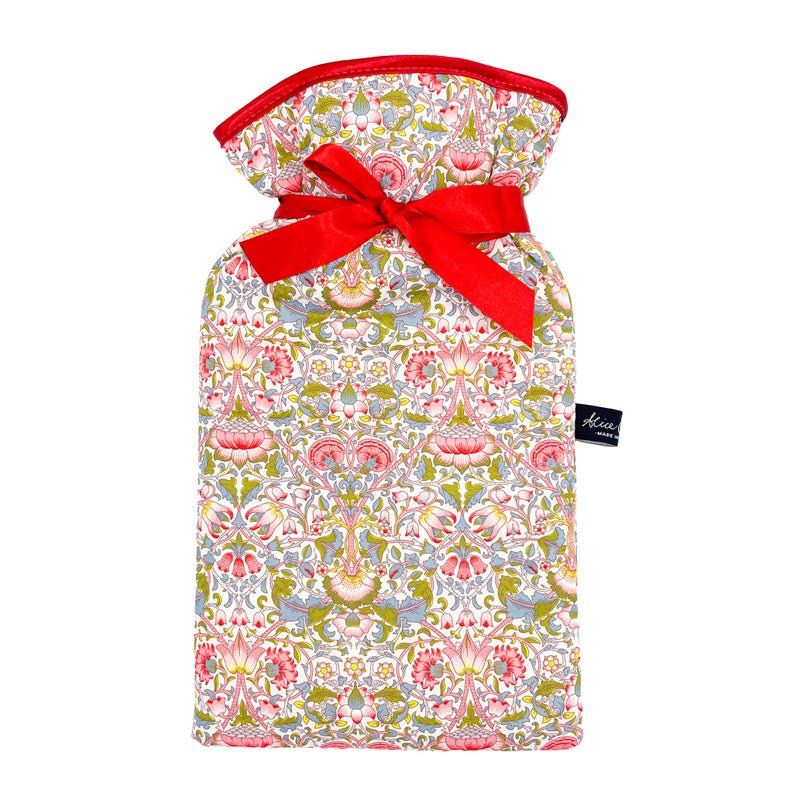 The Alice Caroline Liberty Print Hot Water Bottle features vibrant floral Liberty cotton in pink, green, and yellow, tied with a red ribbon at the neck and finished with an Alice Caroline label on the side.