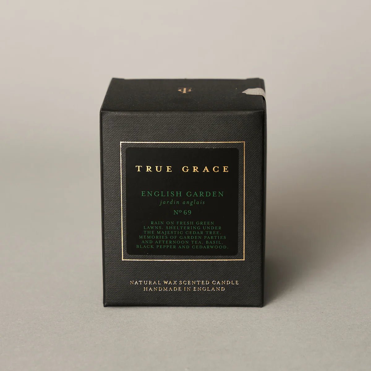 The True Grace English Garden Candle comes in a black box with gold and white text, featuring scents of green lawns, black pepper, and cedarwood. Handmade in Wiltshire from natural wax for a classic English garden ambiance.