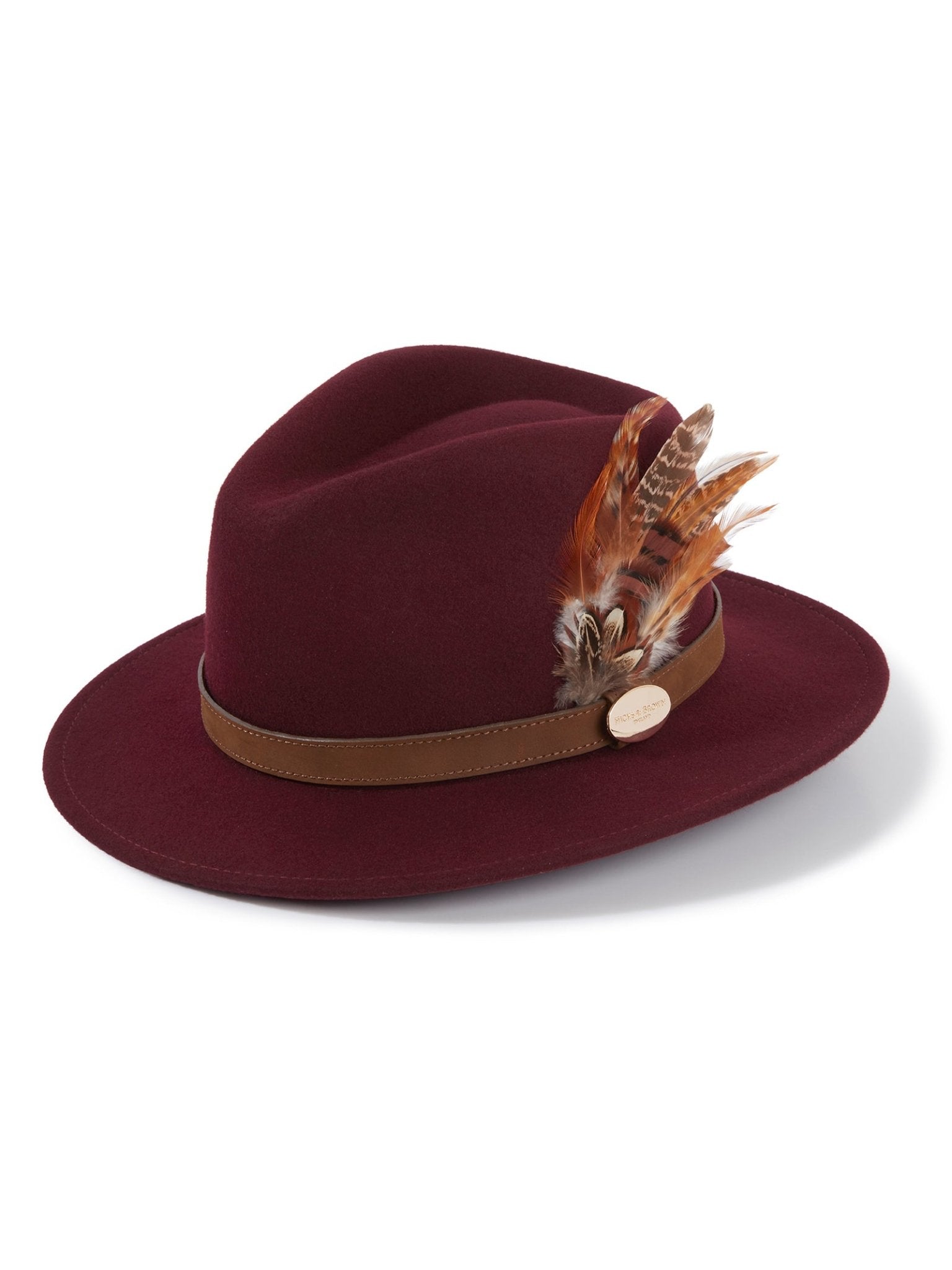 The Hicks & Brown Gamebird Fedora in plum wool felt features a brown leather band, a feather wrap of brown and tan feathers, and is finished with a small gold emblem on the side.