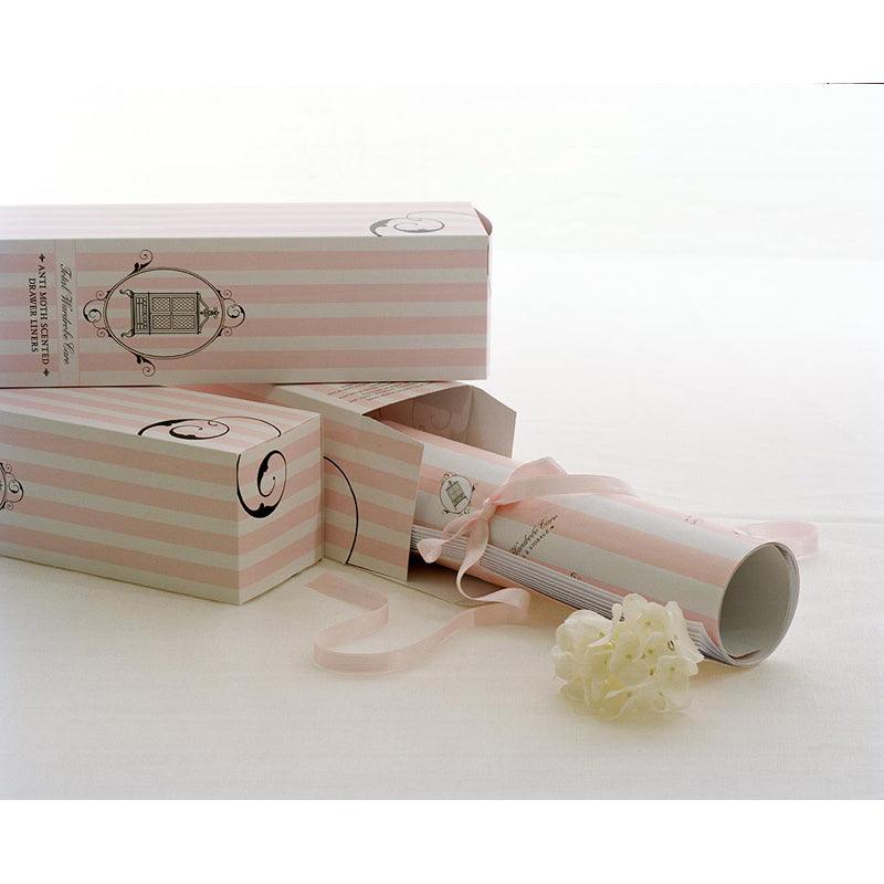 A rolled-up certificate with a cream ribbon and flower sits beside three decorative Total Wardrobe Care Anti-Moth Drawer Liners boxes, ideal for storing or adding gentle fragrance to your drawers.