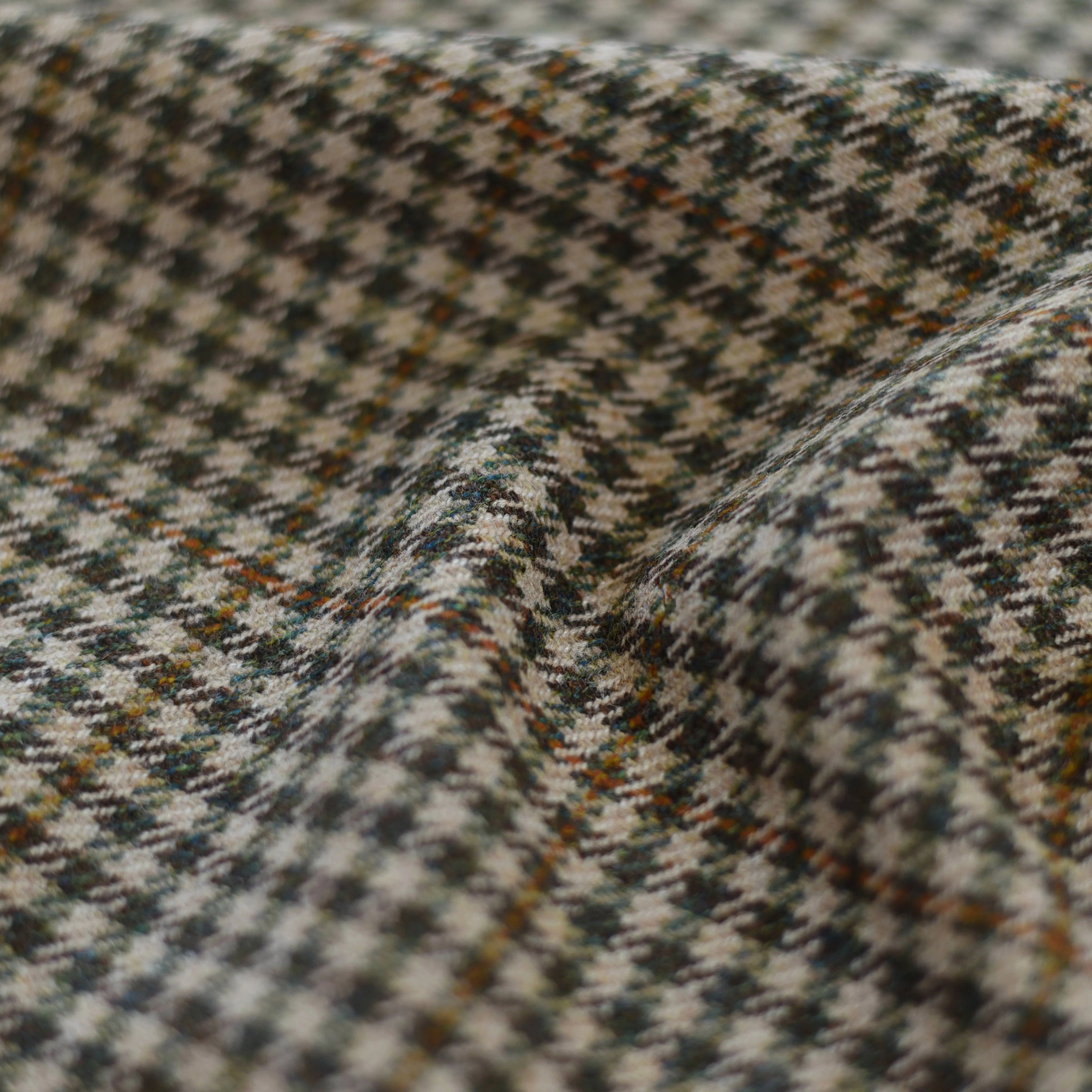 Close-up of House Tweed 71965 by Campbells of Beauly, showcasing a classic houndstooth pattern in black, white, and muted orange on textured Scottish Saxony Tweed with gentle folds and soft shadows.