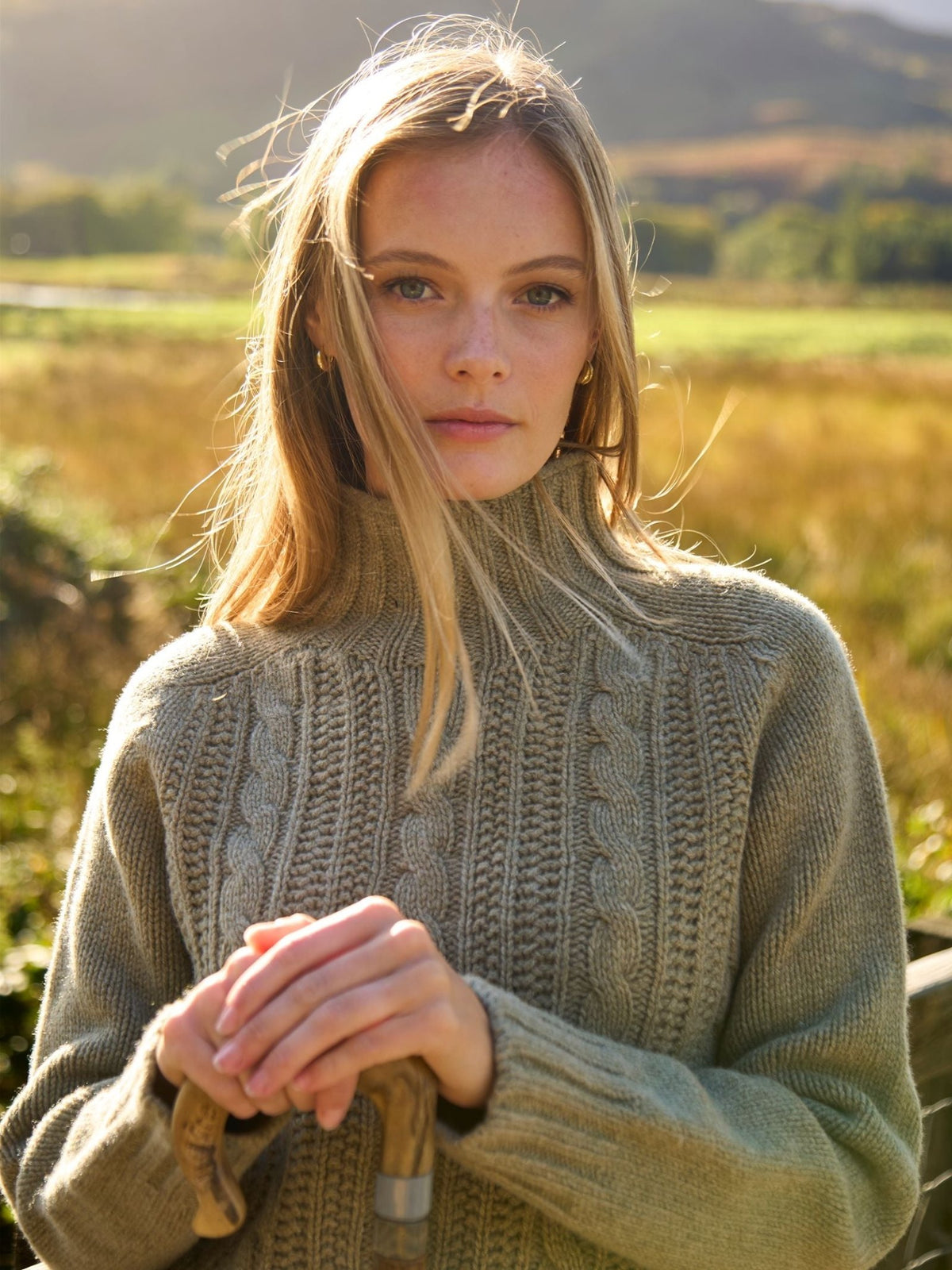Woman wearing a sage green supersoft wool Campbell’s of Beauly Cable Roll Neck Jumper outdoors.