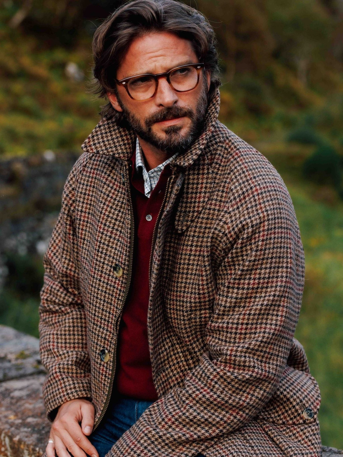 A man wearing a patterned Cannich Coat by Campbell’s of Beauly over a red sweater and checkered shirt.