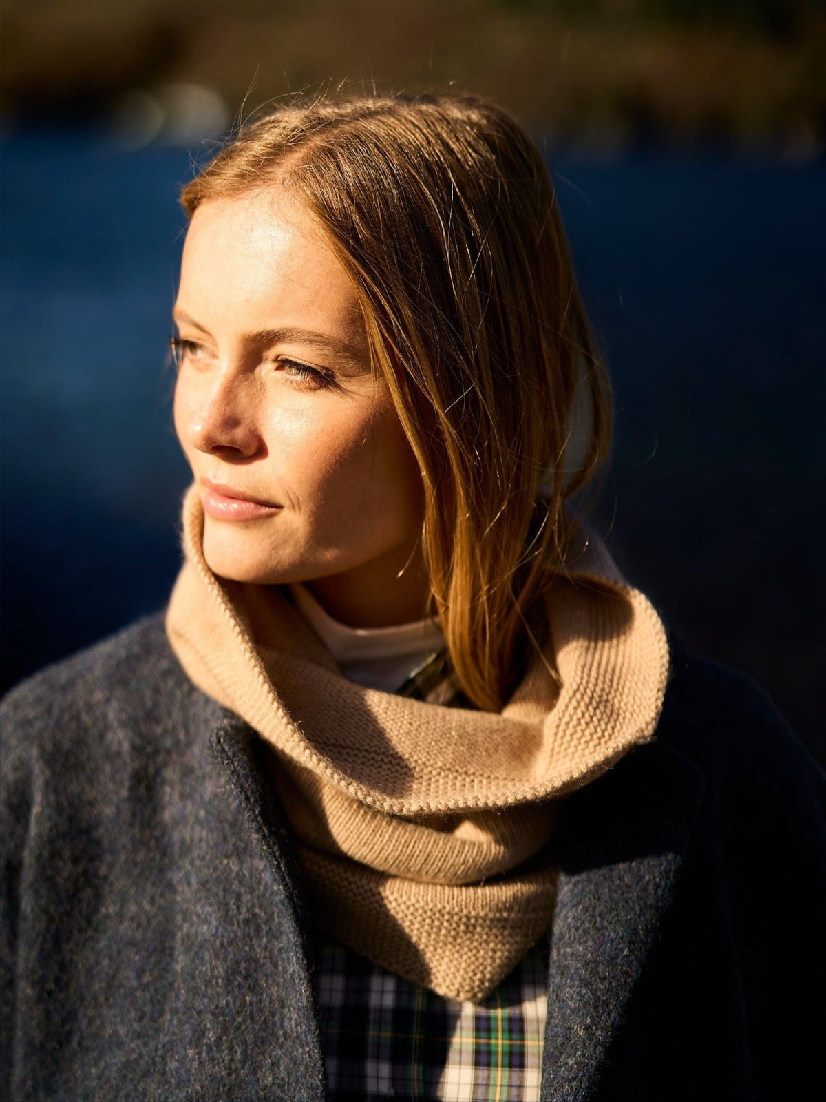 A woman wearing a moss stitch tan Campbell’s of Beauly Cashmere Snood over a plaid shirt and dark coat.