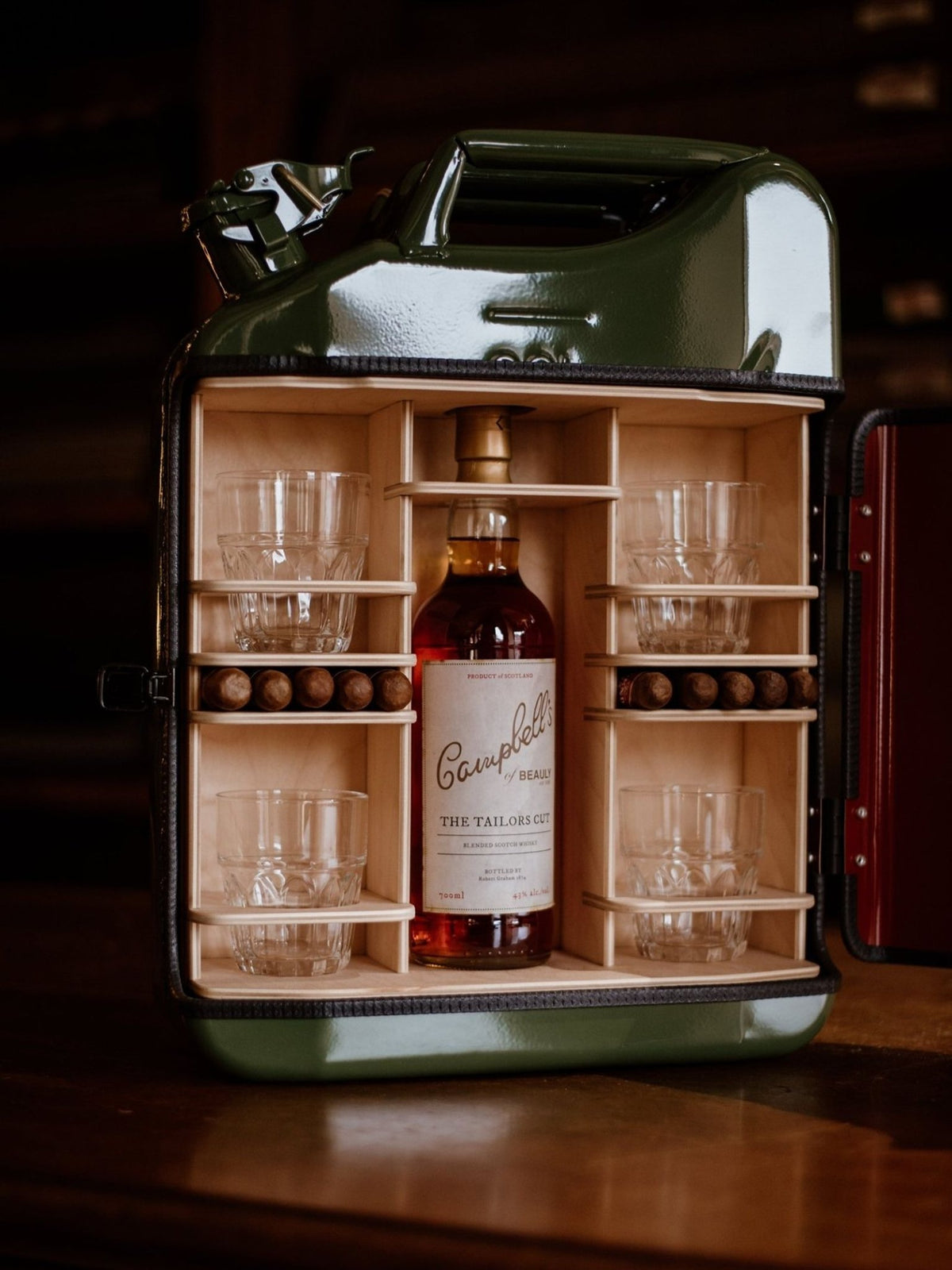 An open, dark green Campbell’s of Beauly Connoisseur Upcycled Mini Bar jerrycan featuring a bottle of whisky, four glasses, and six cigars stored on handmade wooden shelves.