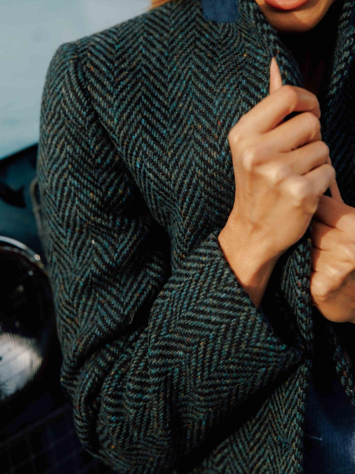 Close-up of a person holding the lapel of a dark green herringbone wool Donegal Herringbone Coat by Campbell’s of Beauly, crafted from classic Donegal tweed.