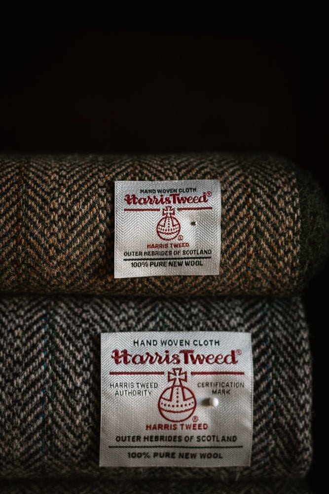 Two brown and green herringbone-patterned House Tweed 95053 jacketing cloths from Campbell’s of Beauly, each featuring a white label with the iconic Harris Tweed orb logo and text certifying their authenticity as genuine hand-woven Scottish cloth.