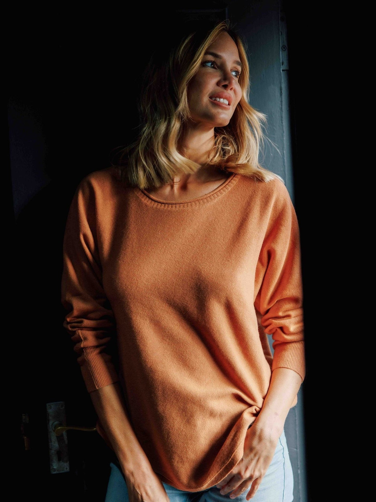 A woman wearing a peach-colored Campbell’s of Beauly Merino Cashmere Boat Neck Jumper, featuring a long-sleeved Italian knit design.
