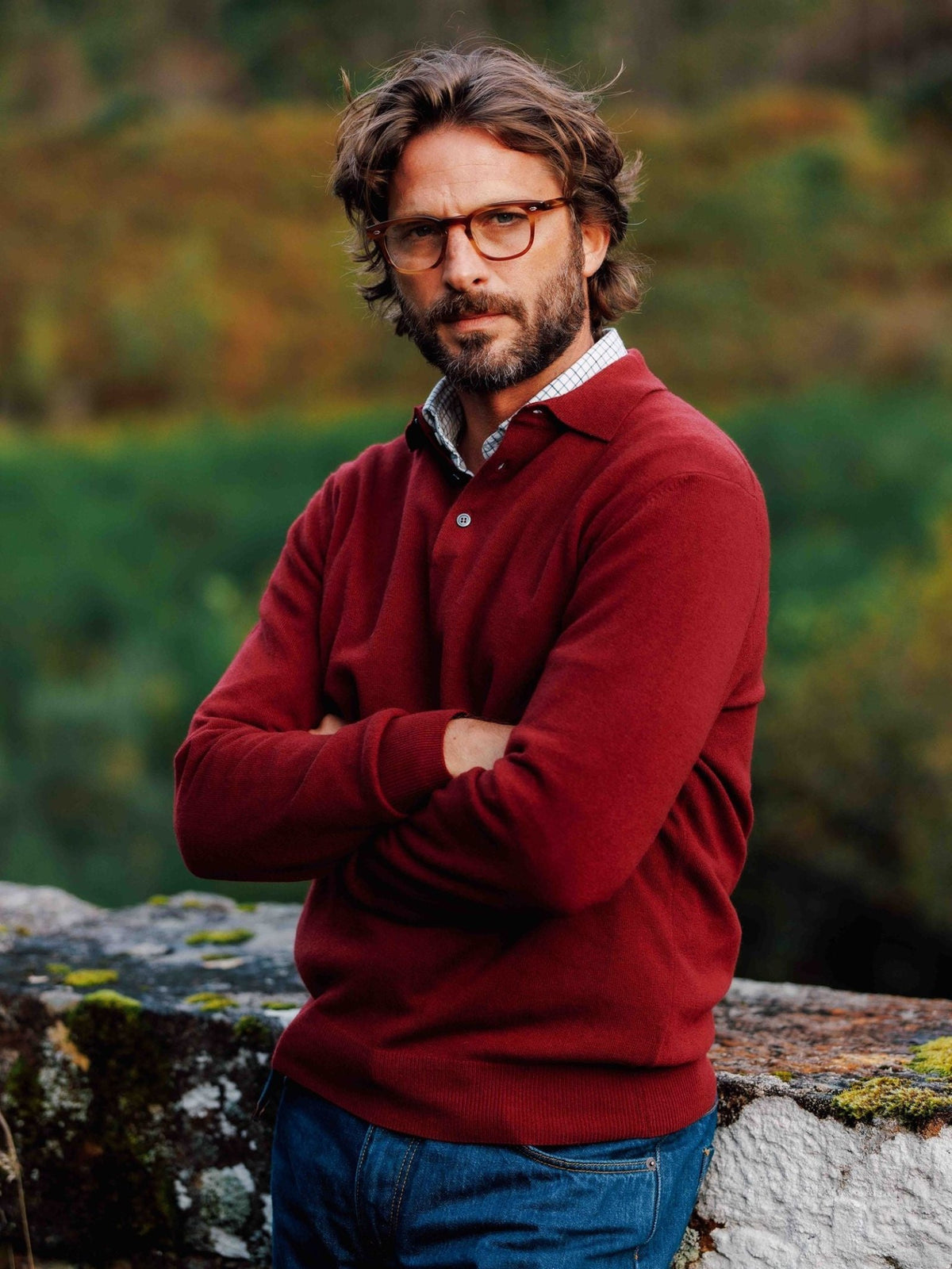 A man stands outdoors with his arms crossed, wearing a burgundy Merino & Cashmere Rugby with a plaid collar.