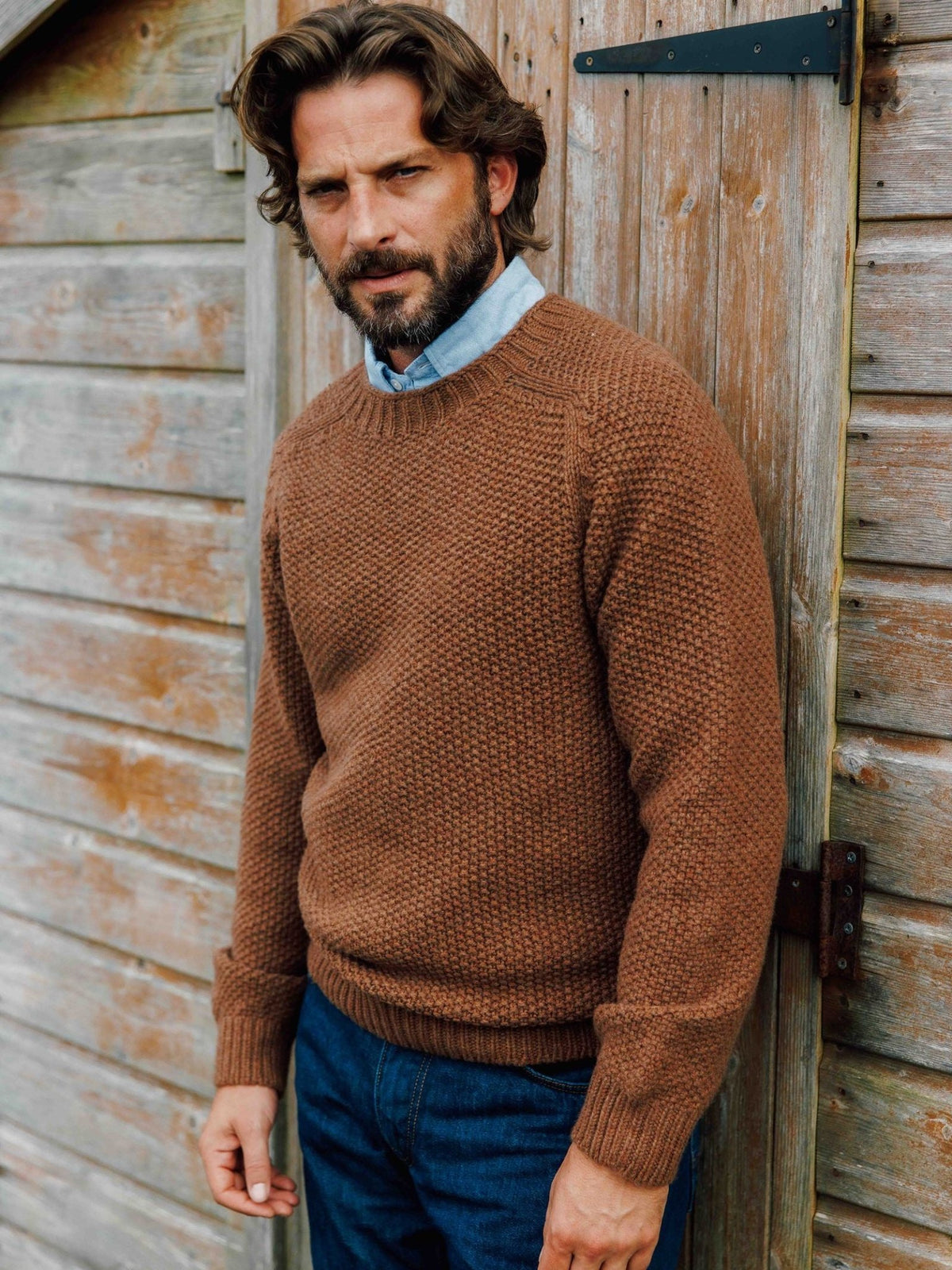 A man wearing a Campbell’s of Beauly Moss Stitch Crew Neck Jumper over a light blue collared shirt and blue jeans.