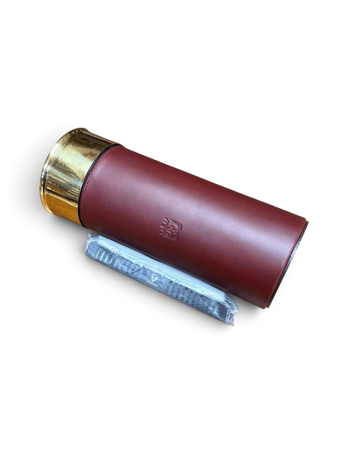 A cylindrical brown leather Rey Pavón Shotgun Cartridge Cigar Humidor with a gold cap and cedar-lined interior lies next to a wrapped black item on a white background.