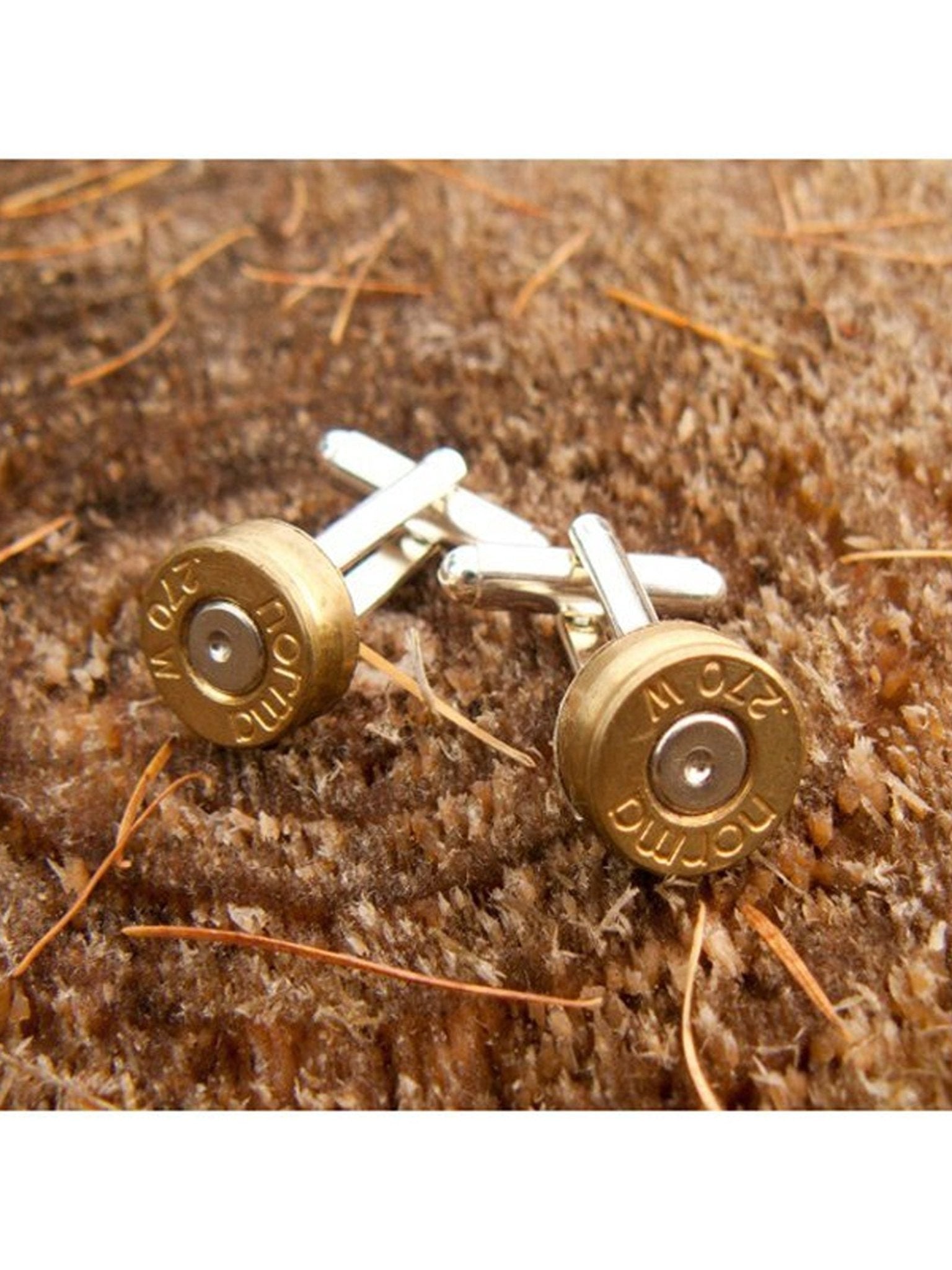 A pair of Campbell’s of Beauly Silver-Plated Bullet Cufflinks rests on a brown textured surface with scattered straw-like fibers—an ideal gift for shooting enthusiasts.