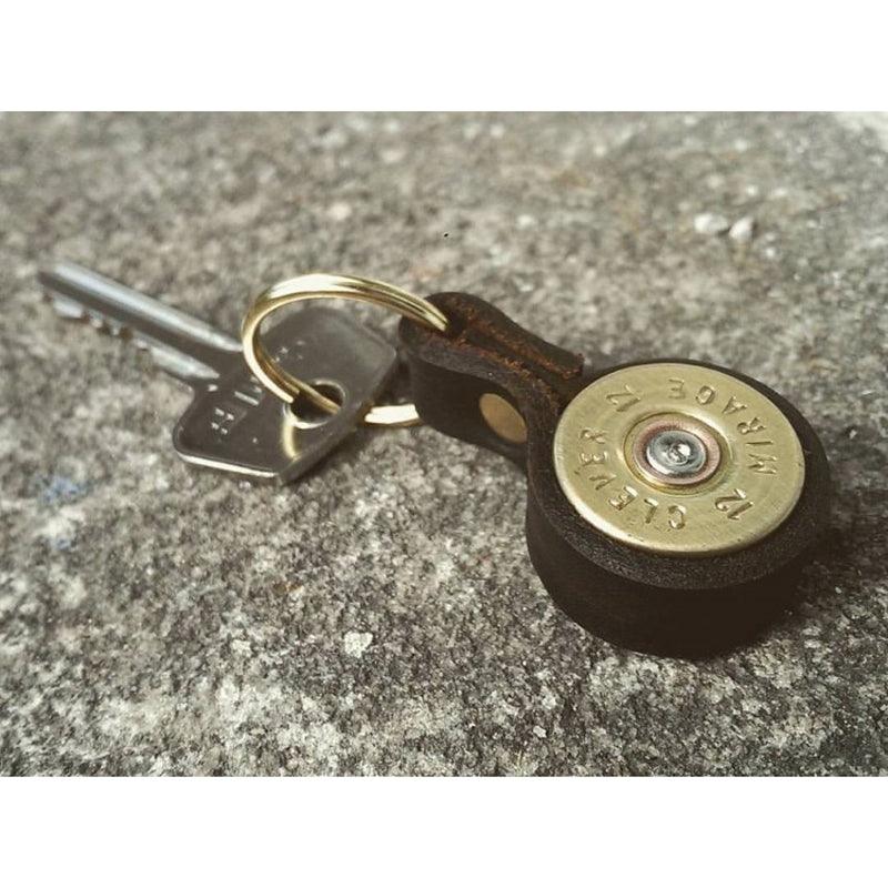 The Cartridge Keyring by Campbells of Beauly, crafted from a spent brass shell casing and leather, rests on rough gray concrete—a unique handcrafted gift and stylish country sports accessory.