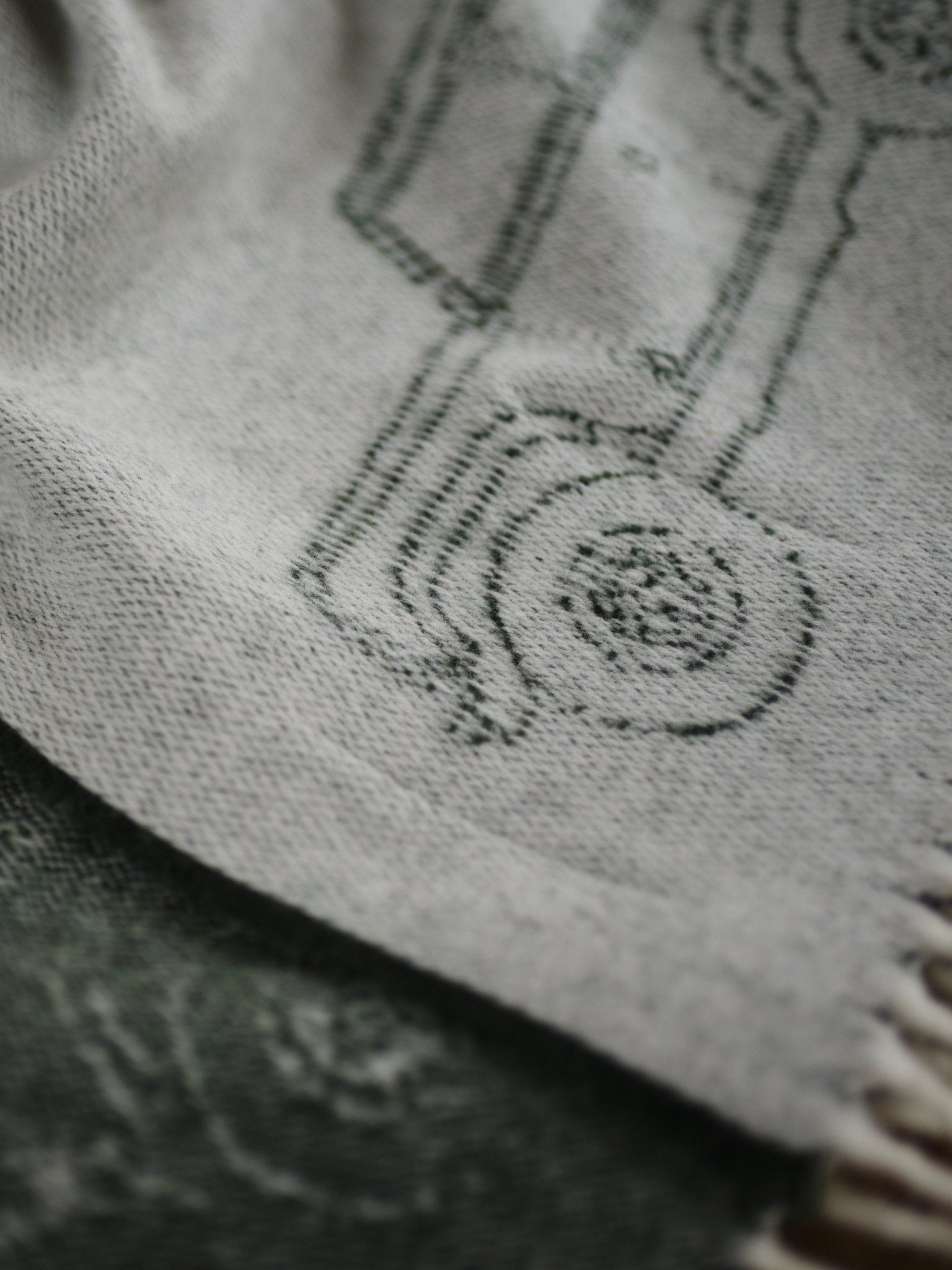 A close-up of the Land Rover Defender Jacquard Throw by Campbells of Beauly shows its light wool, visible texture, subtle dark outline of a wheel and vehicle part, and fringed edges.