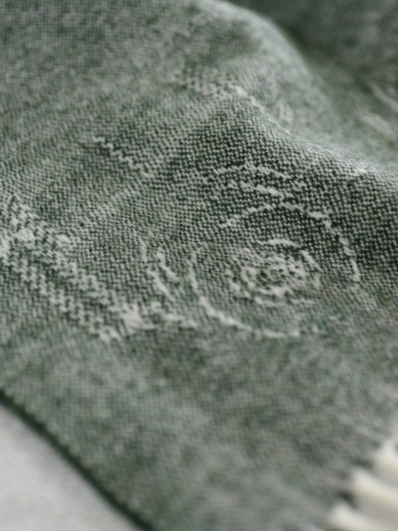 Close-up of the Land Rover Defender Jacquard Throw by Campbells of Beauly: textured green fabric with a subtle woven swirl pattern and visible fibers, evoking a classic British wool blanket with rich light and shadow.