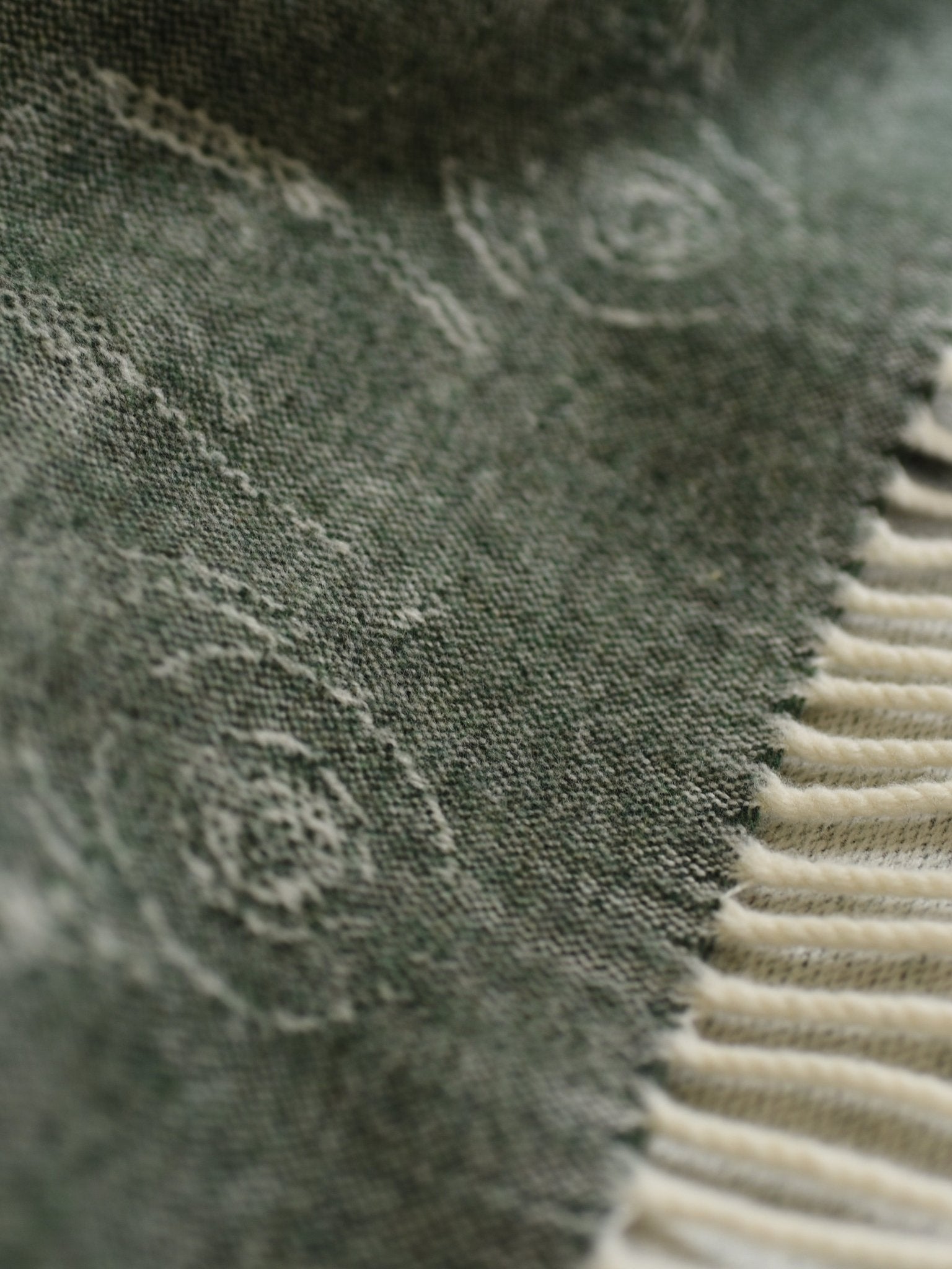 Close-up of textured green fabric with a subtle swirl and frayed edges beside cream ribbed material—details from the Campbells of Beauly Land Rover Defender Jacquard Throw, a classic British wool blanket.