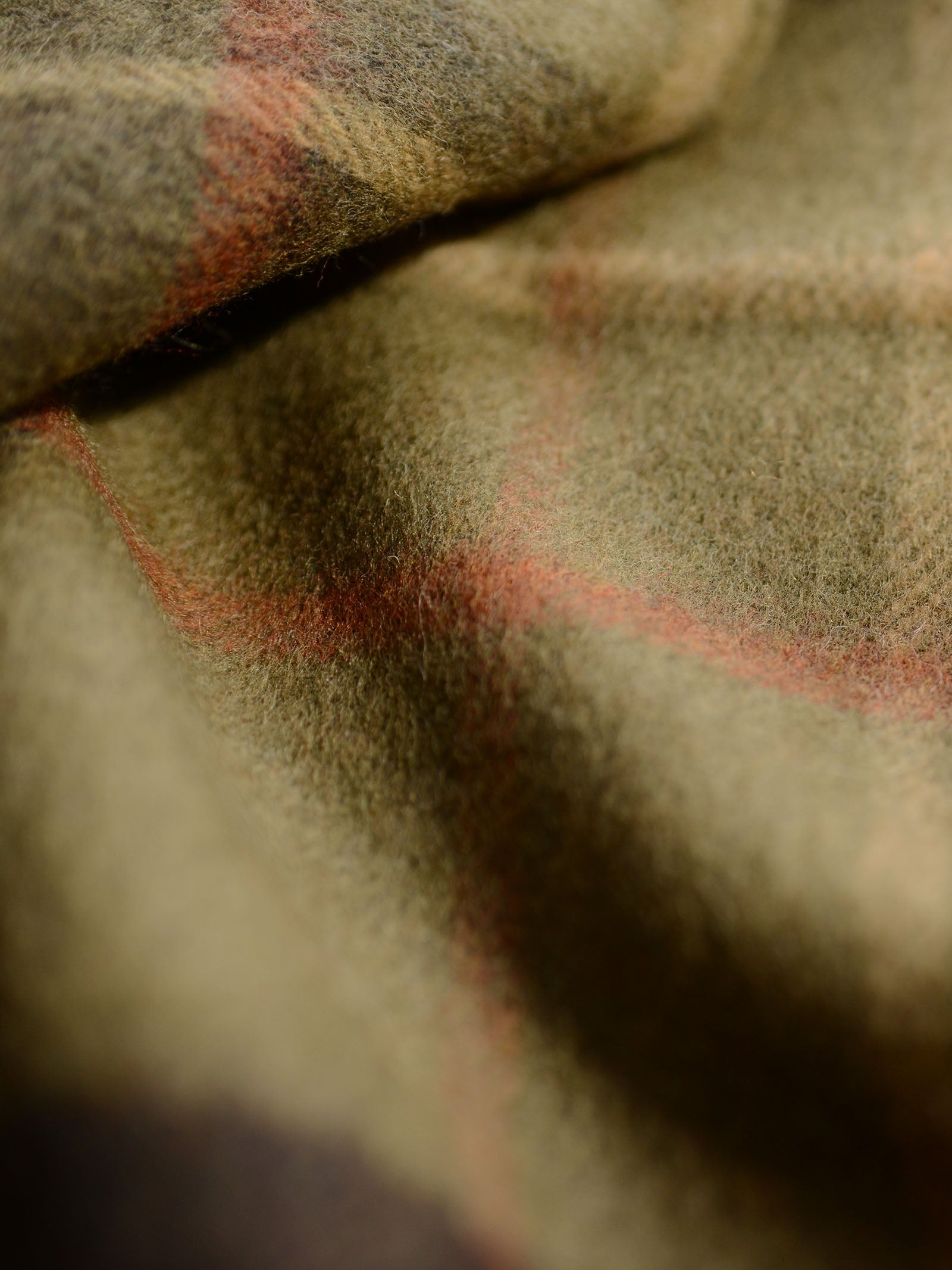 Close-up of the Glassburn Merino Throw by Campbell's of Beauly, featuring soft wool in a subtle olive green plaid with red lines, showing its cosy folds and textured surface.