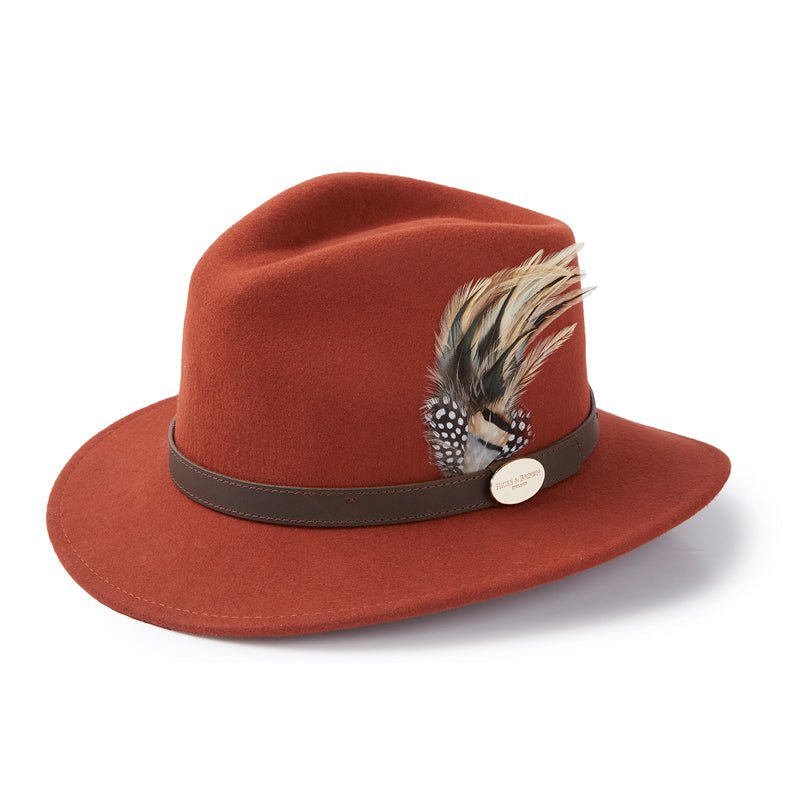 The Hicks & Brown Guinea & Pheasant Feather Cinnamon Fedora features a cinnamon color, brown band, feather accents, and a small gold oval emblem for an elegant touch.