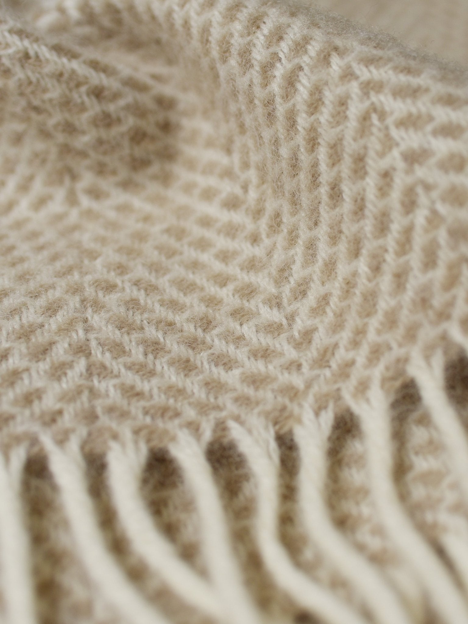 Close-up of the Stipled Twill Blanket by Campbells of Beauly in beige, featuring a herringbone pattern and fringed edges. The soft, breathable weave highlights its cozy, textured appearance.