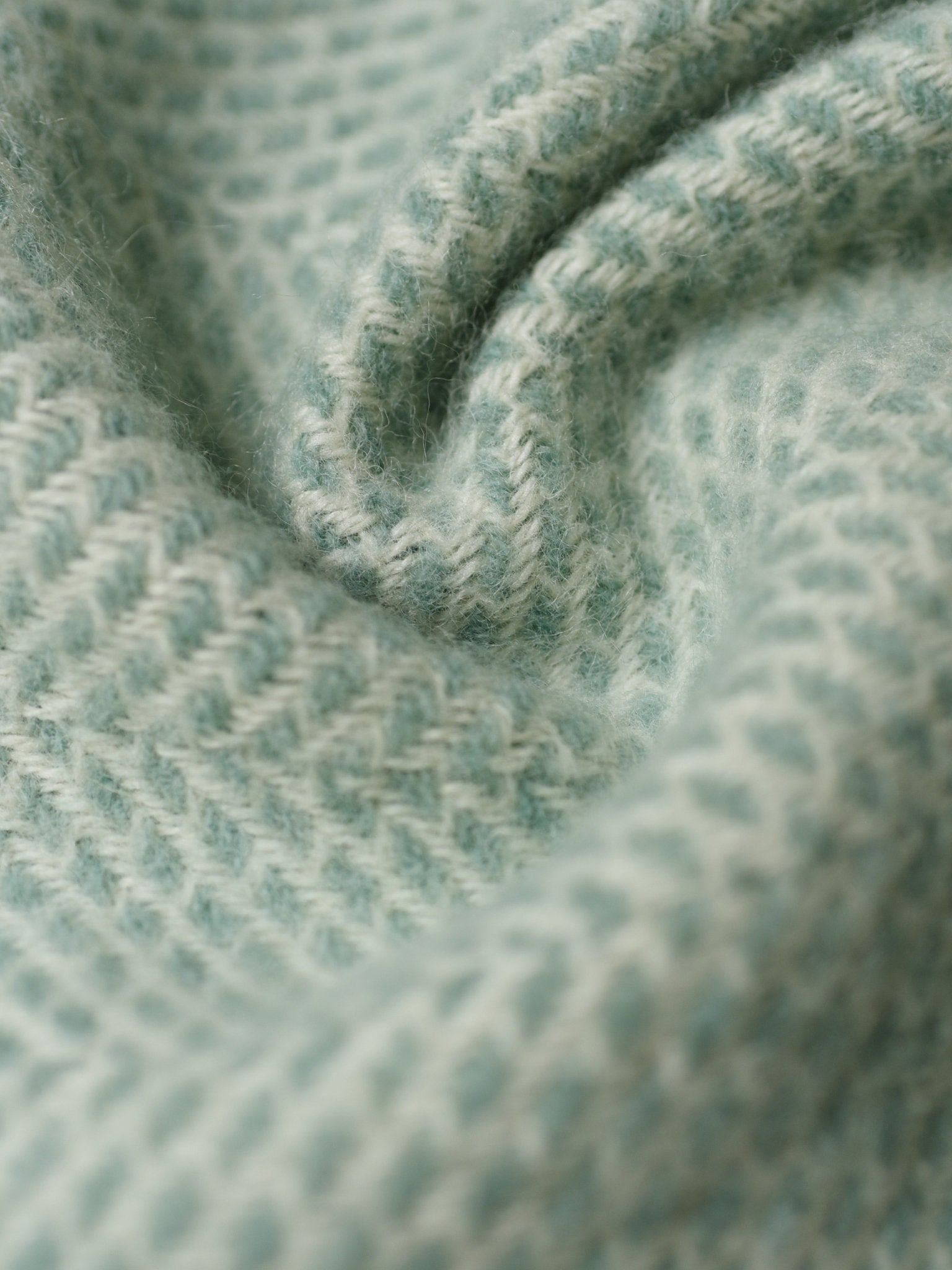 Close-up of the Stipled Twill Blanket by Campbells of Beauly in soft, light blue wool with a subtle herringbone pattern and gentle folds, highlighting the elegance of this breathable, lightweight twill design.