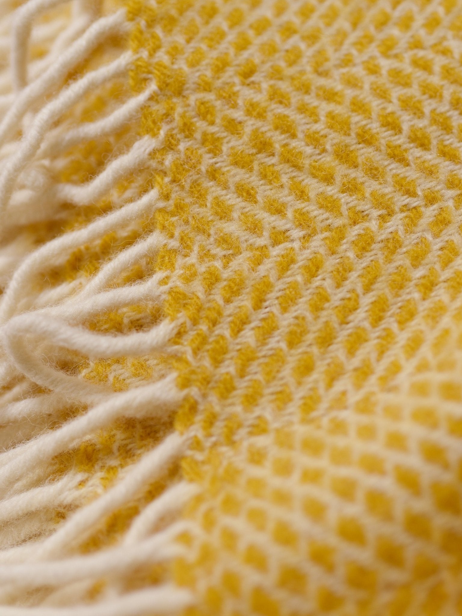 Close-up of the Stipled Twill Blanket by Campbells of Beauly, featuring a soft, breathable weave with a yellow and white diamond pattern and fringed edges.