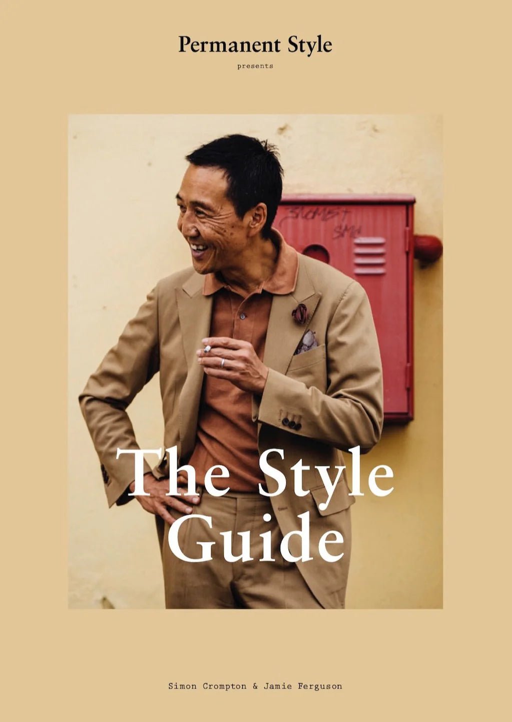 A man in a tan suit and rust polo smiles before a yellow wall with a red mailbox, embodying contemporary menswear. The cover displays Permanent Styles The Style Guide by Simon Crompton & Jamie Ferguson.