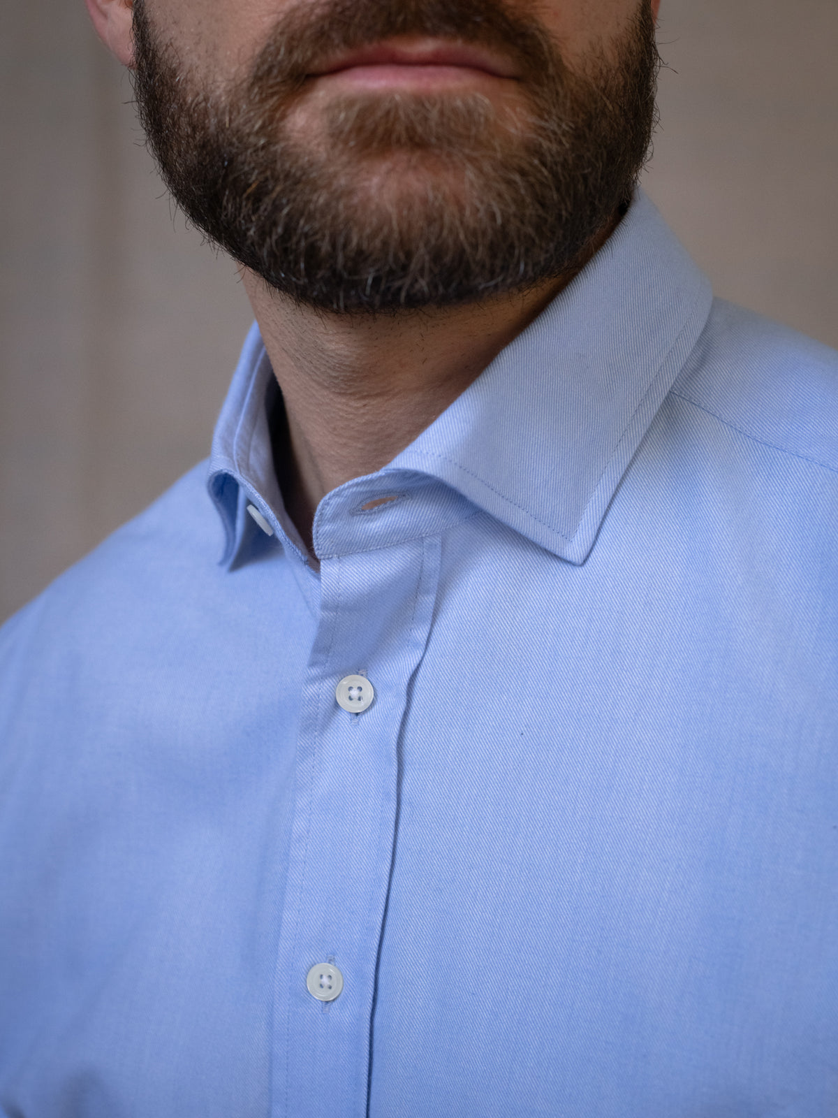 A close-up of a man wearing the Campbell’s of Beauly Twill Shirt in light blue classic fit, highlighting his neatly trimmed beard and part of his face against a neutral background.