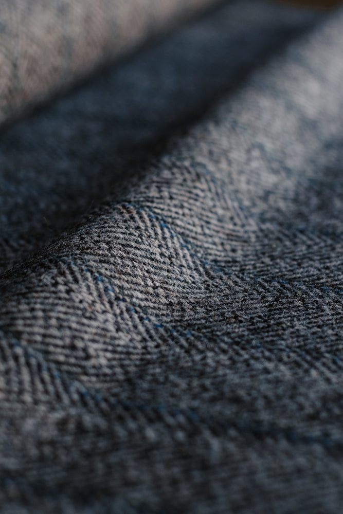 Close-up of Campbell’s of Beauly House Tweed 95053, featuring blue and gray herringbone patterned fabric with soft lighting and visible texture that highlights the detailed weave and subtle color variations characteristic of classic jacketing cloth.