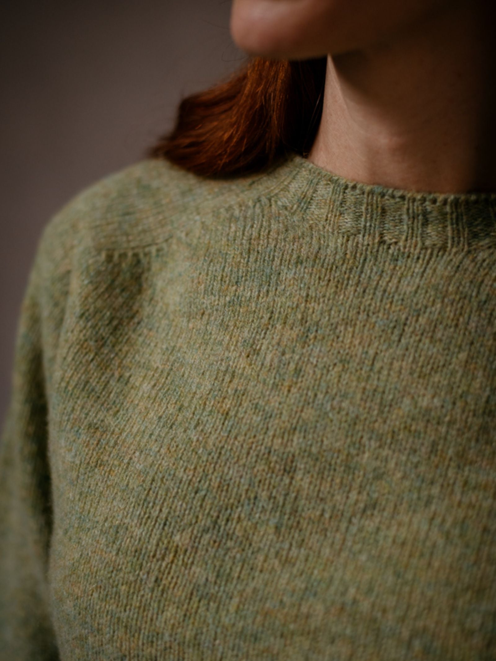 A close-up shows a person in a textured, light green Cropped Shetland Jumper by Campbells of Beauly, highlighting the neck, shoulder, and upper chest with softly lit reddish-brown hair.