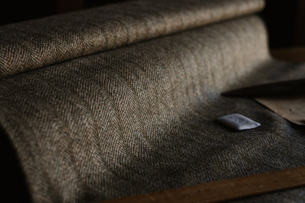 A close-up of a roll of Campbell’s of Beauly House Tweed 95054 fabric on a table, accompanied by a ruler, tailor’s chalk, and brown paper nearby, all softly side-lit—a timeless setting for crafting fine jacketing cloth.