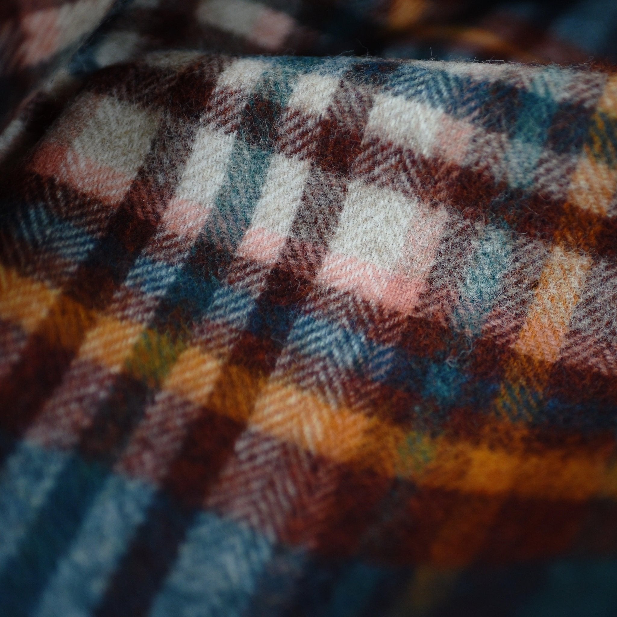 Close-up of the Auld Stock Abriachan Lambswool Throw by Campbell's of Beauly, featuring a soft plaid in blue, brown, orange, cream, and pink. The blurred fibers and warm texture evoke the cozy comfort of a Yorkshire-inspired blanket.
