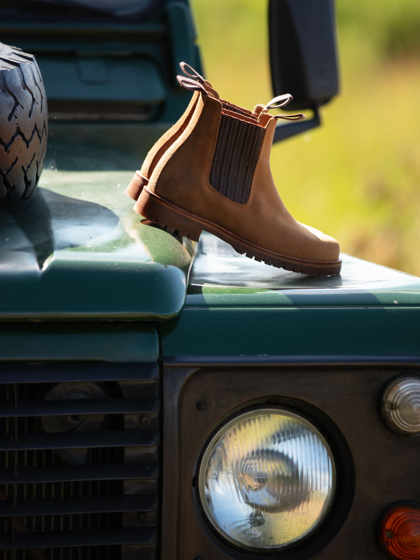 A single Campbell's of Beauly Leather Chelsea Boot, crafted from premium leather, sits on a green vehicle’s hood beside a headlight and spare tire—an essential, timeless piece for any country wardrobe.