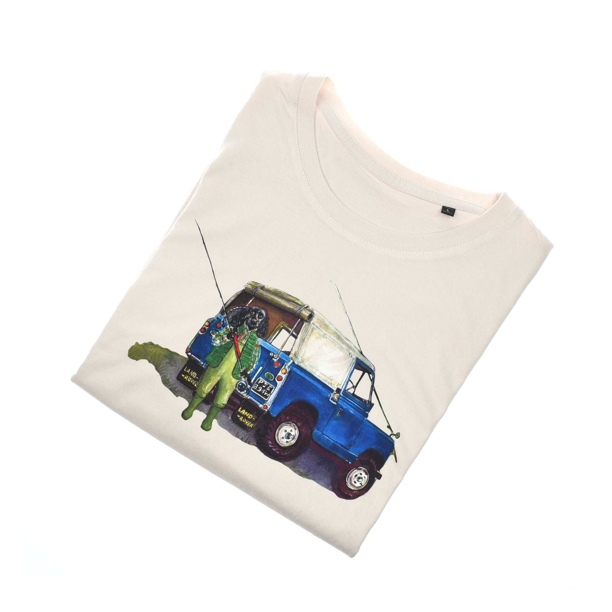 The Land Rover Cocker T-Shirt by Campbells of Beauly is cream-colored and neatly folded. Its front displays a Sophie Murray illustration: a blue vintage Land Rover on grass with a person in green waders holding fishing rods.