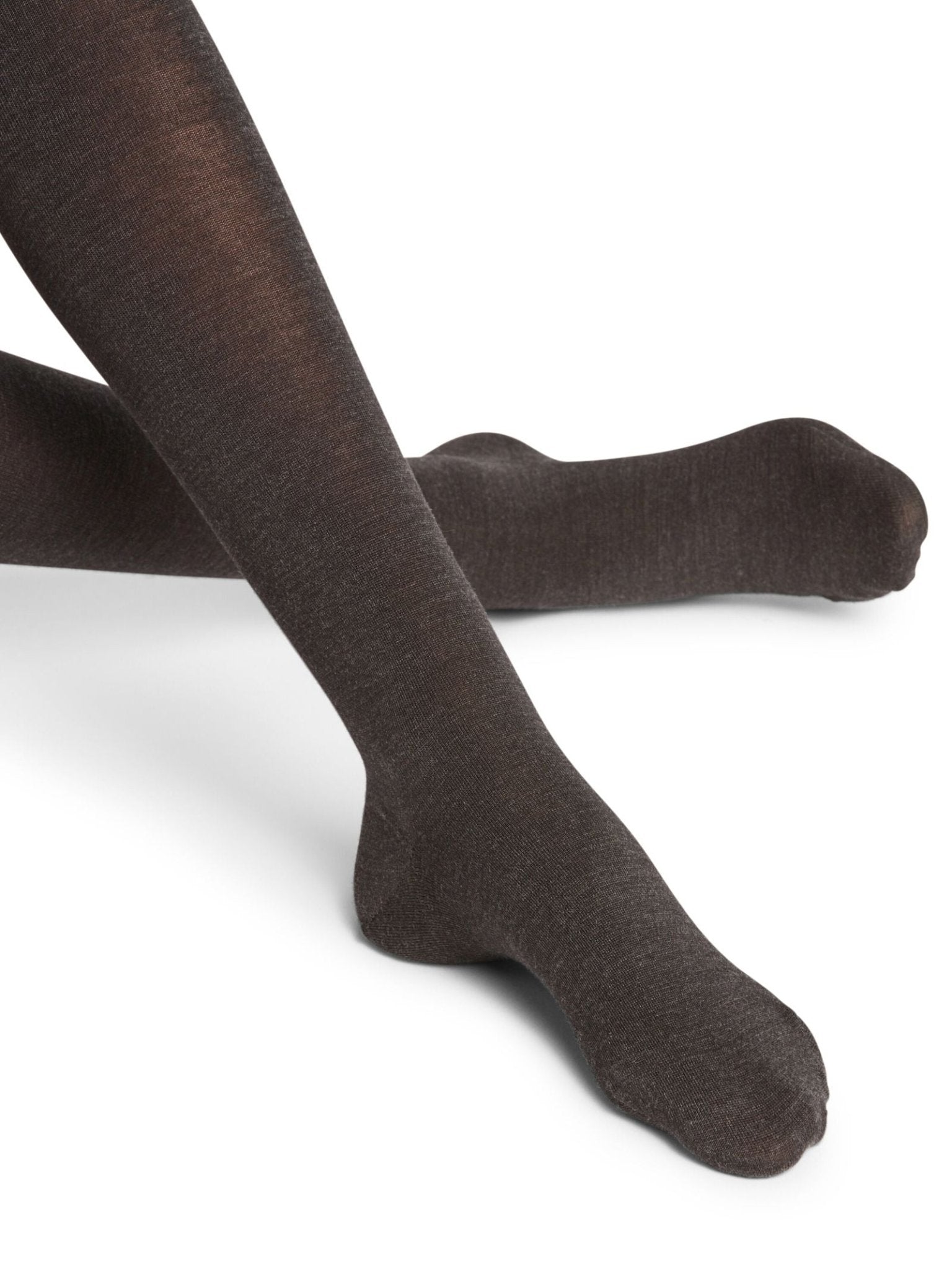 A person wearing opaque, anthracite FALKE Merino Tights sits with legs crossed at the ankles against a white background.