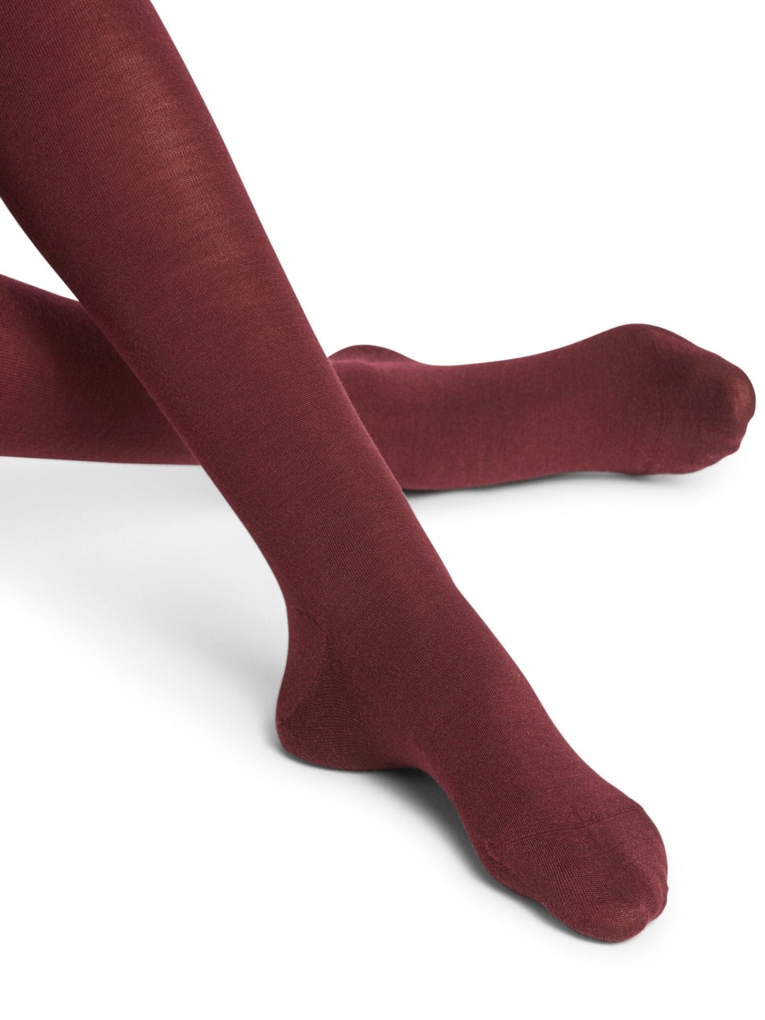 A person wearing FALKE Merino Tights in Barolo crosses their legs with feet slightly outward against a plain white background.