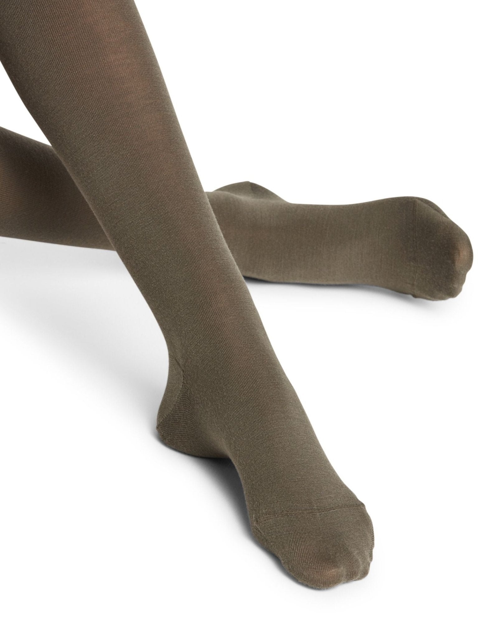 A close-up of crossed legs wearing FALKE Merino Tights in Military Green, showing the lower legs and feet without shoes against a white background.