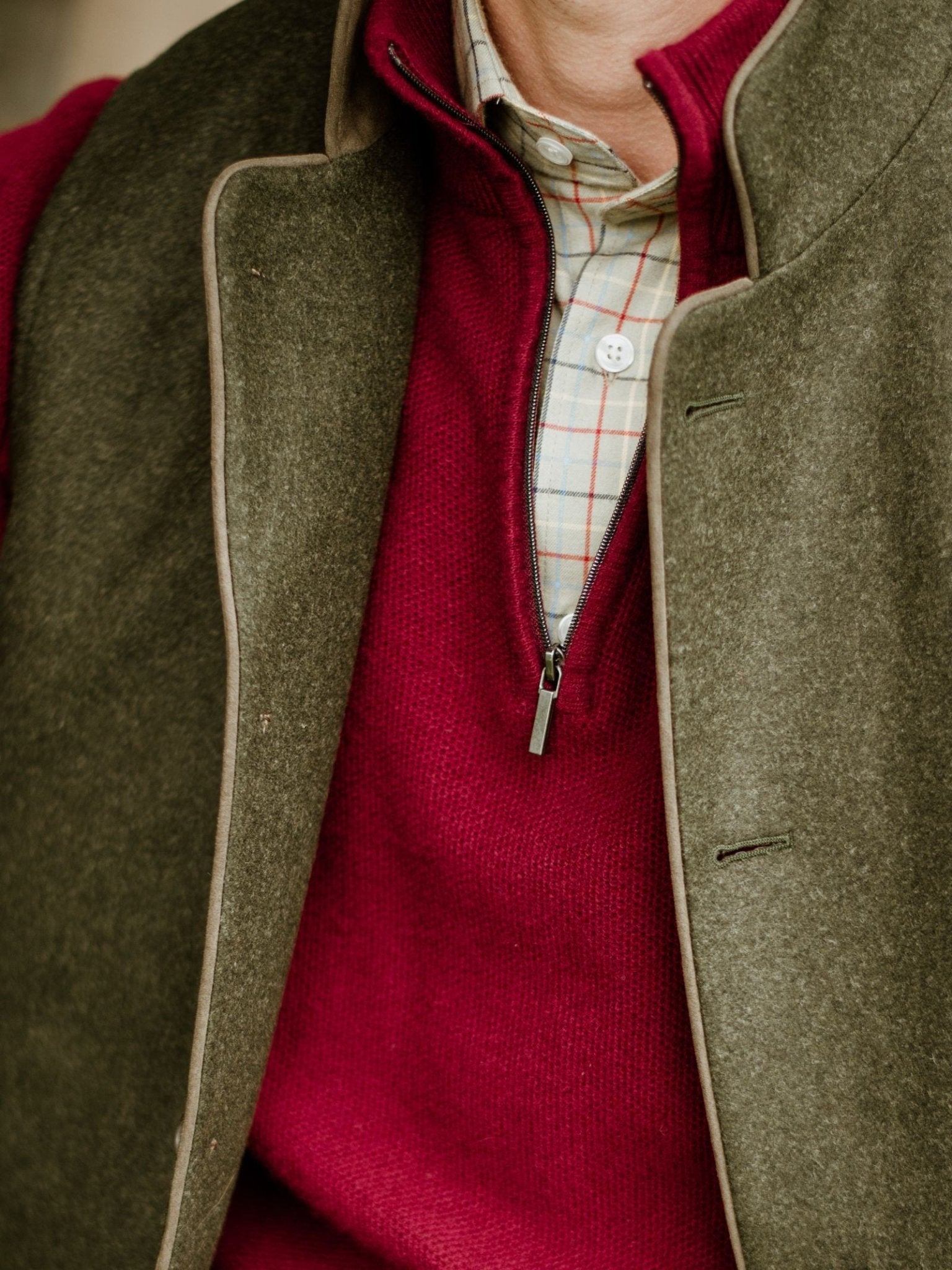 A close-up of a person layering the Campbell's of Beauly Luxury Nehru Gilet over a red half-zip sweater and a light plaid button-up shirt.