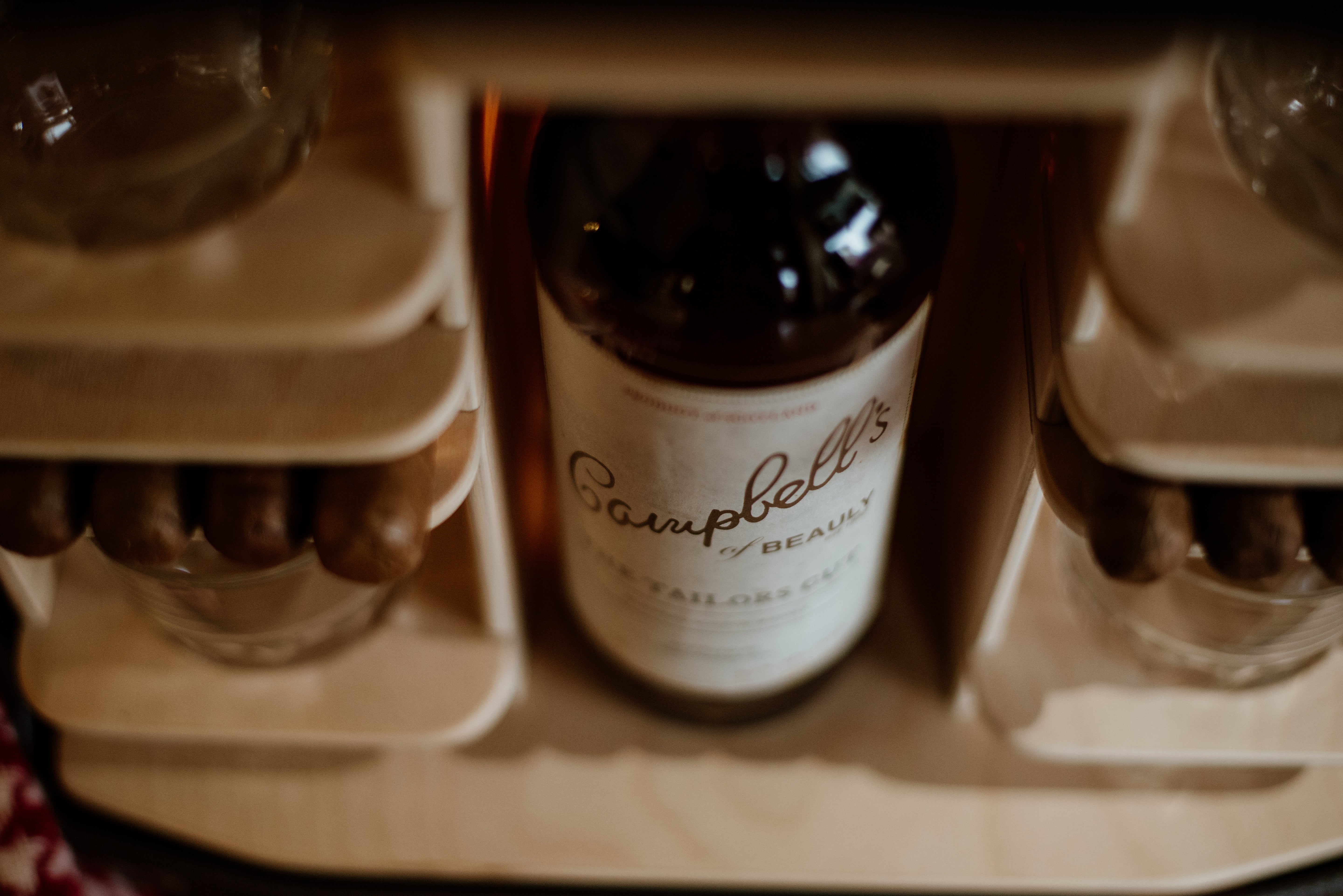 A Campbells of Beauly bottle sits in the Connoisseur Upcycled Mini Bar’s wooden holder, surrounded by glass cups and cigars. The overhead shot highlights the label, evoking warm, ambient light and a cozy, rustic vibe.