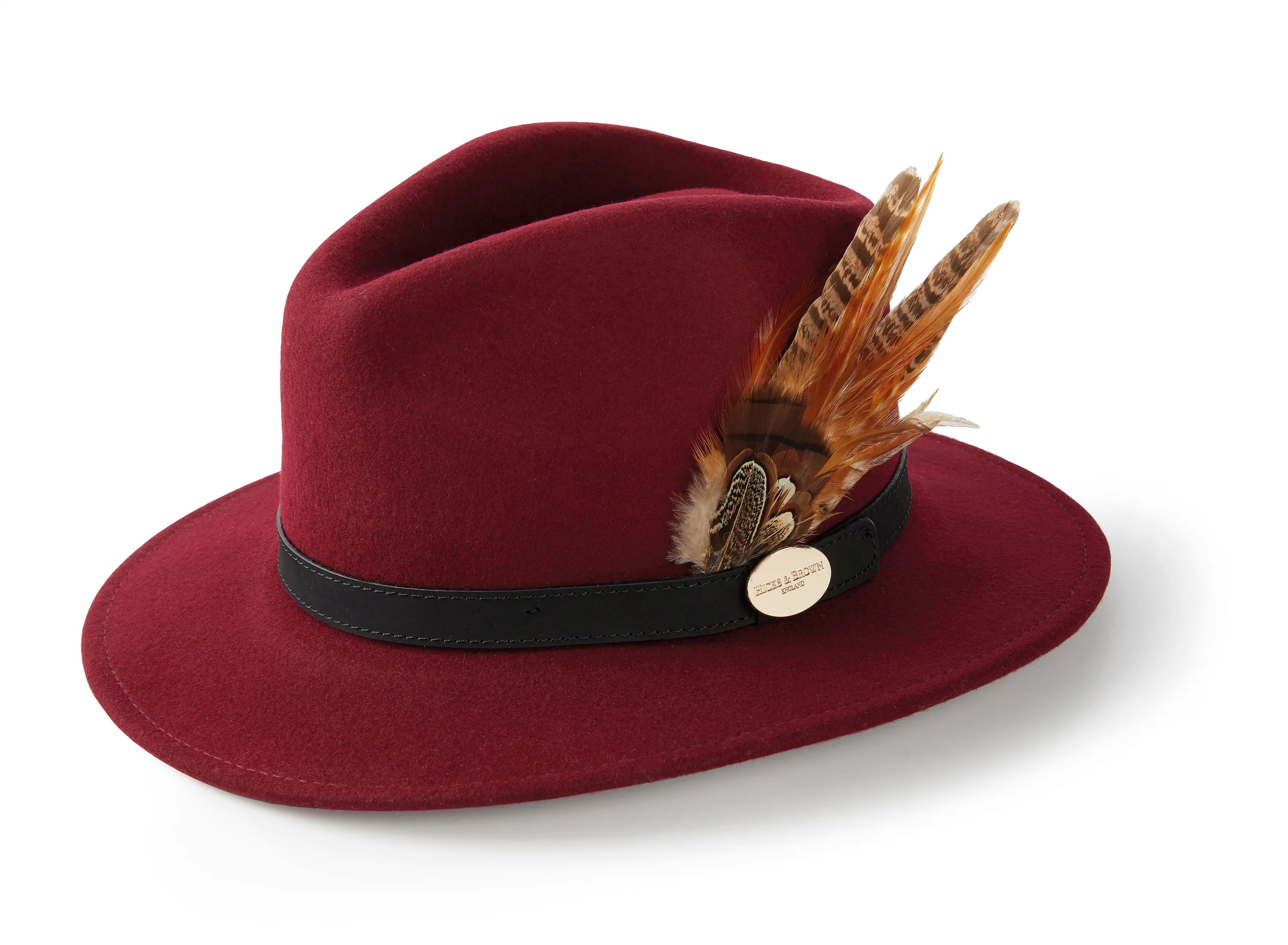 The Hicks & Brown Gamebird Fedora is a maroon wool felt hat with a black band, finished with a brown and orange feather wrap and a round gold pin on the side.